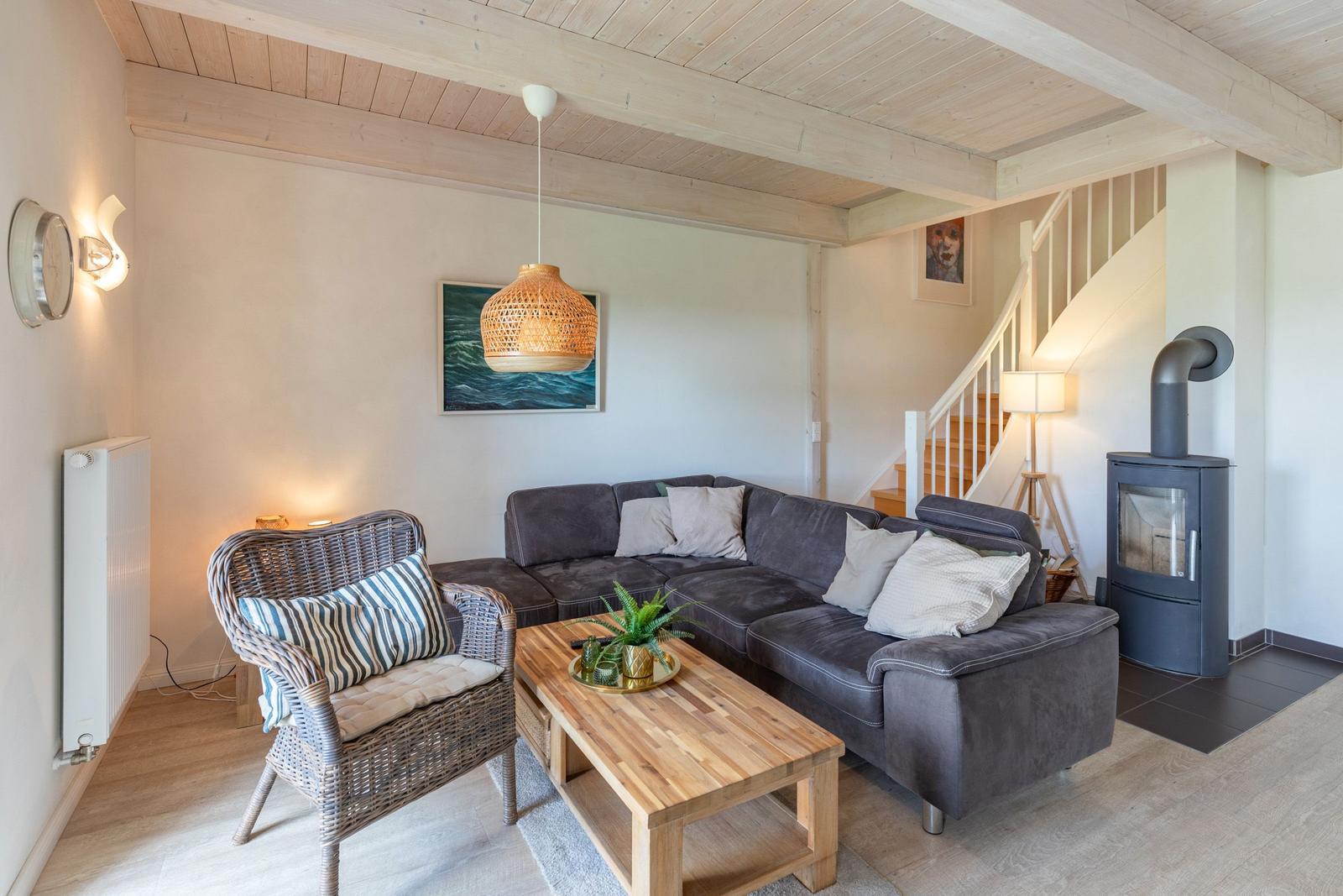 Living room with sofa, armchair, and wood-burning stove. Visible wooden ceiling and staircase.