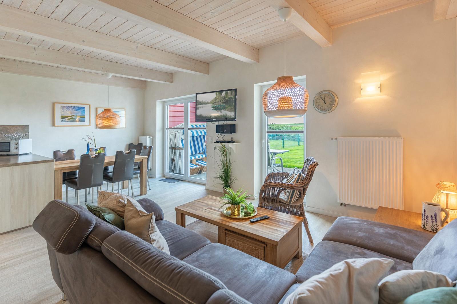 Living and dining area with sofa, dining table, and TV. Access to terrace with garden view.