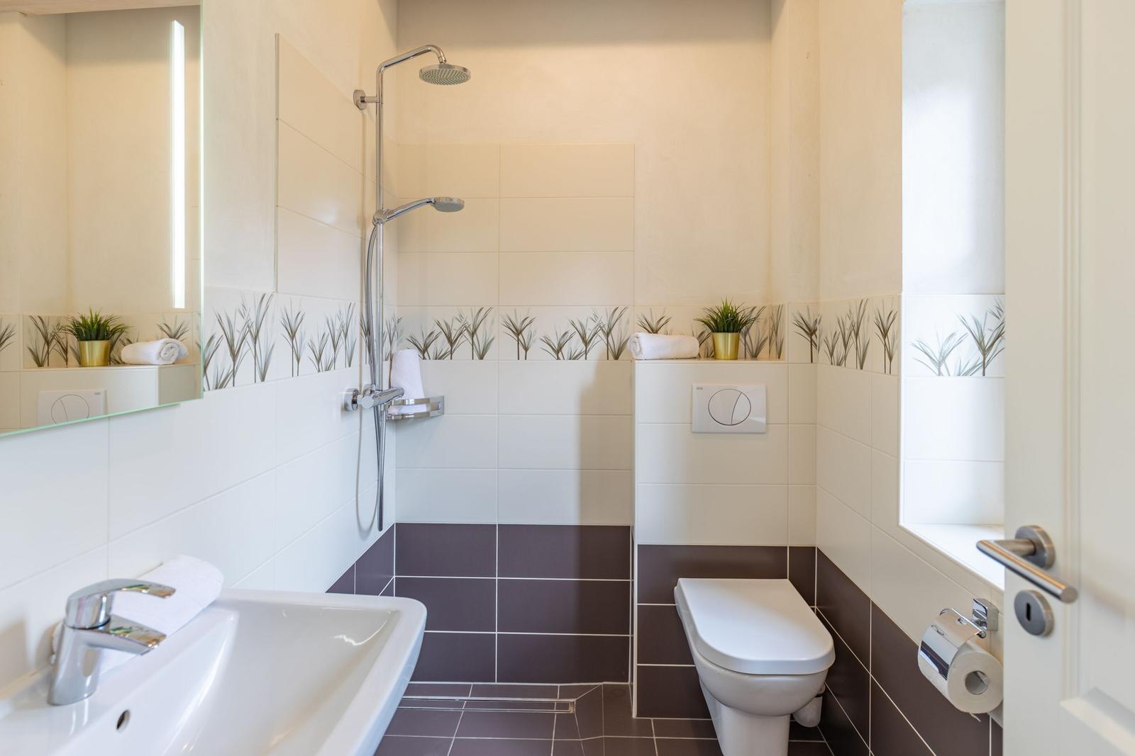 Bathroom with shower, sink, and toilet. Tiles with plant motif.