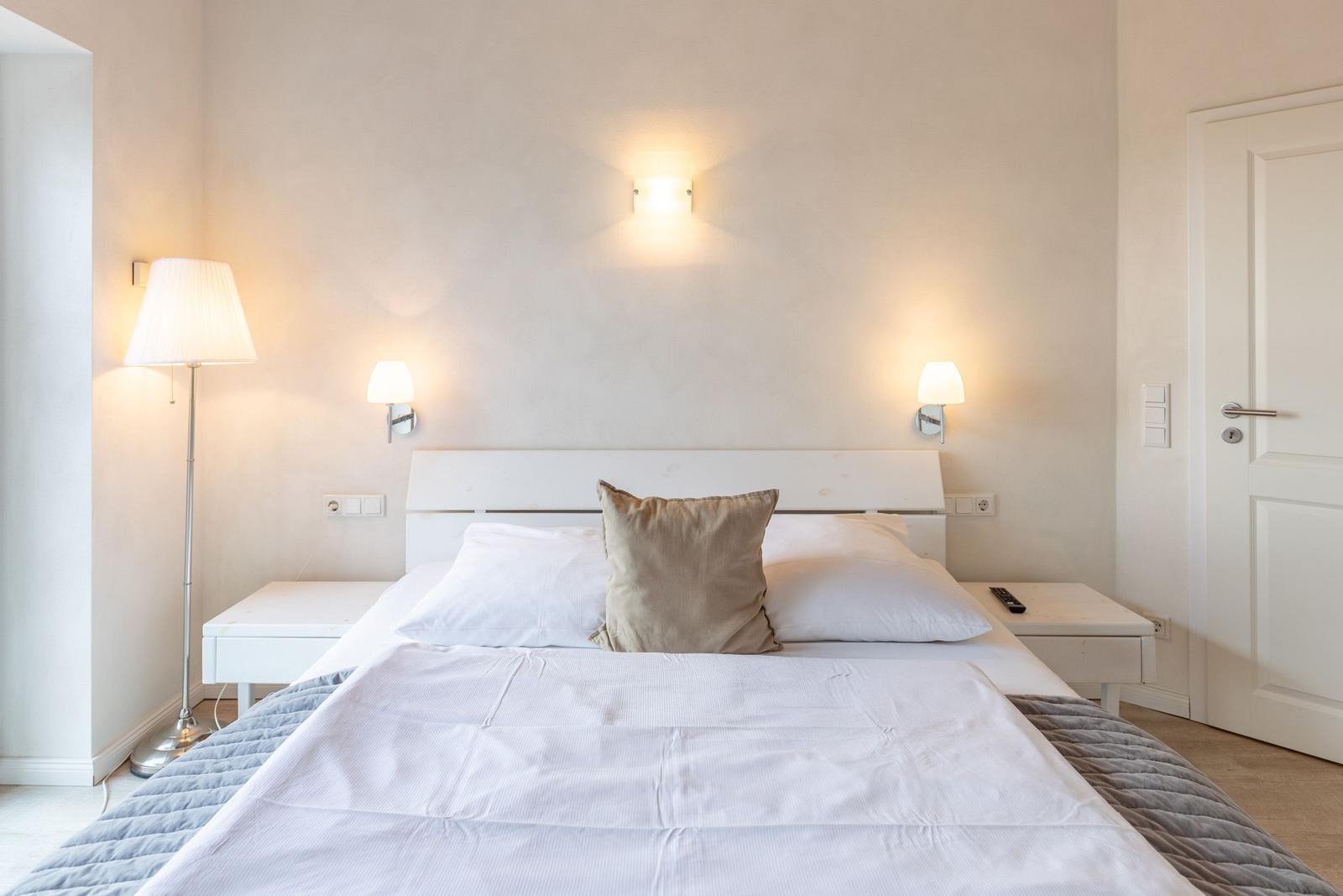 Bedroom with white bed, nightstands, and wall lamps.