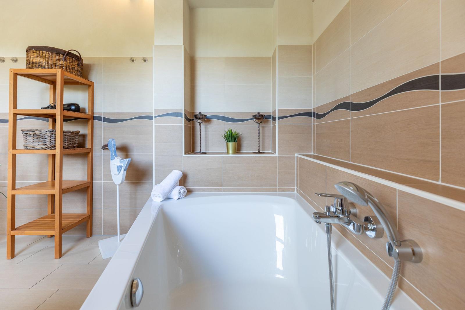 Bath with bathtub, wooden shelf, and decorative items on the wall.