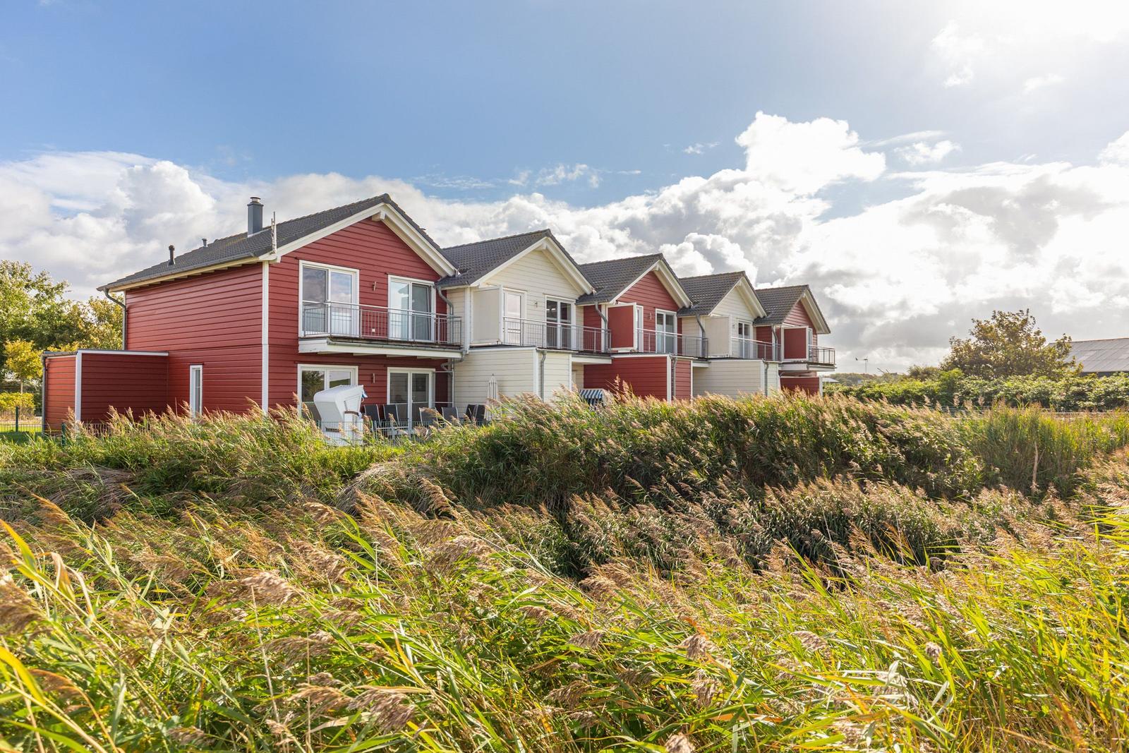 Red and white vacation homes with balconies behind tall grass.