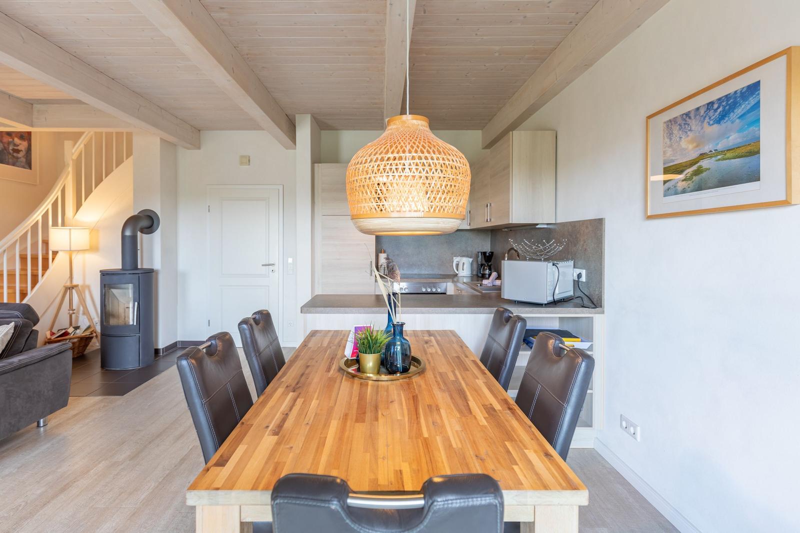 Dining area with wooden table and chairs, kitchen and fireplace in background.