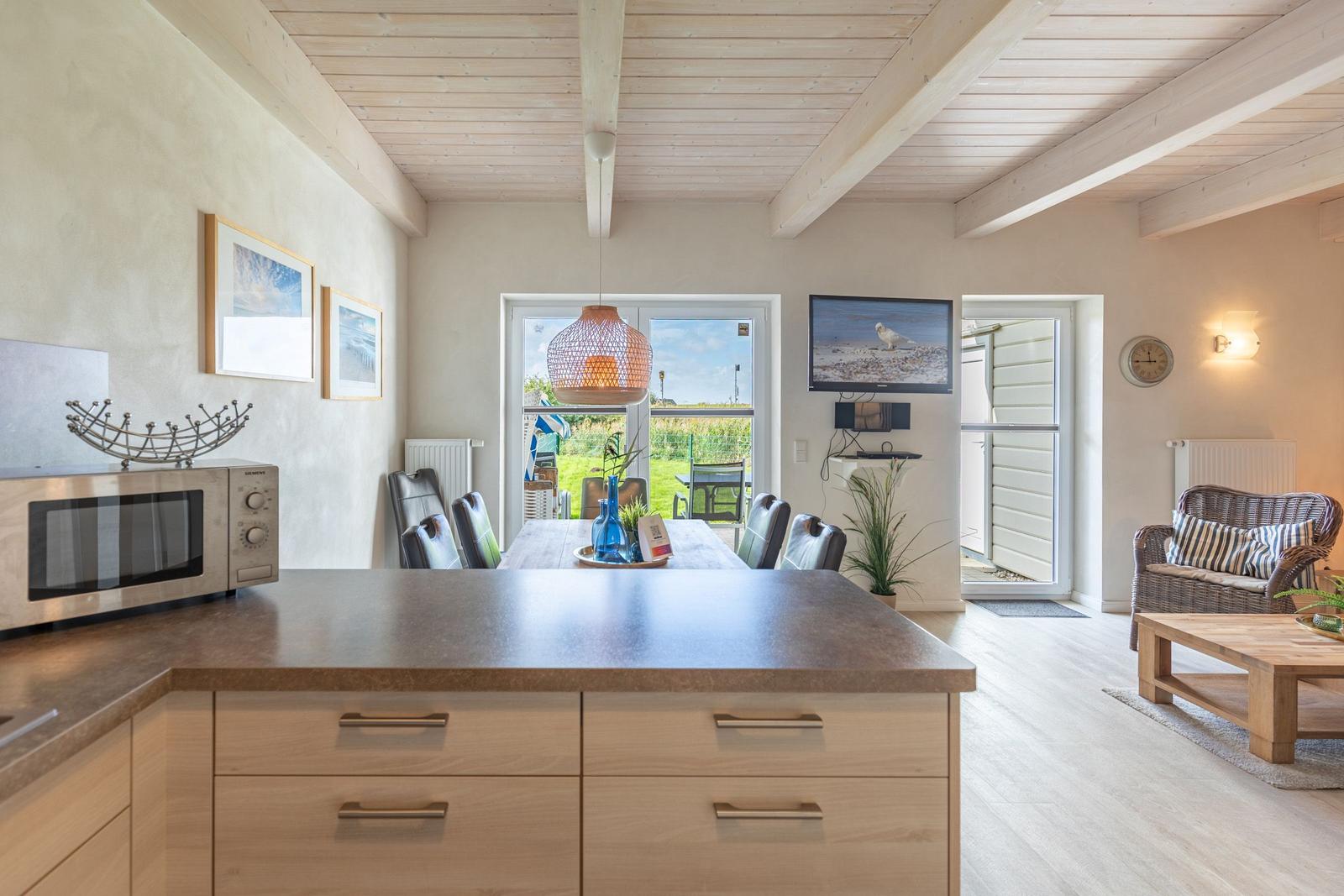 Kitchen with dining table, living room with sofa and TV. Wooden ceiling and terrace door.