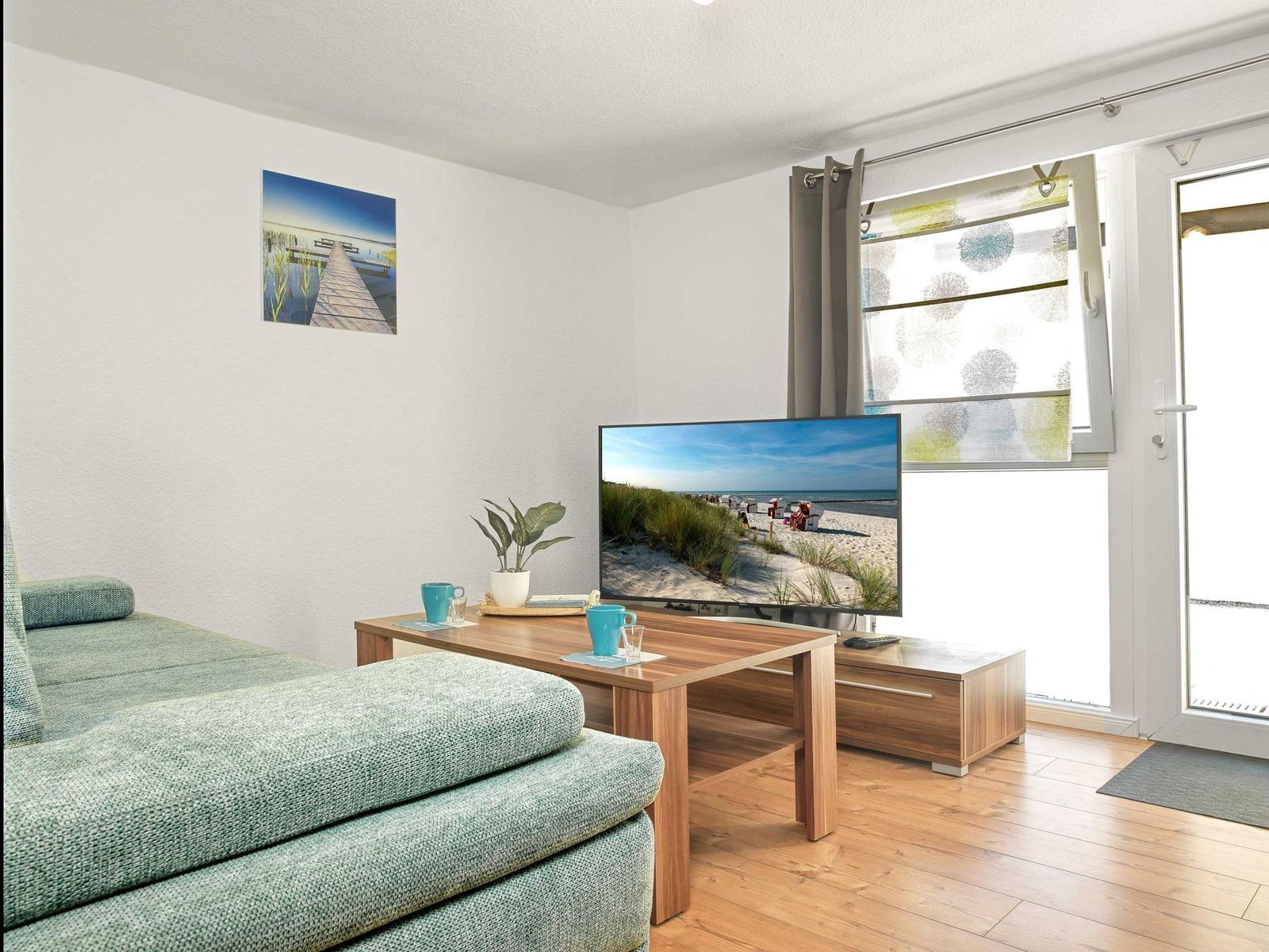 Wohnzimmer mit Sofa, TV und Fenster zur Terrasse.