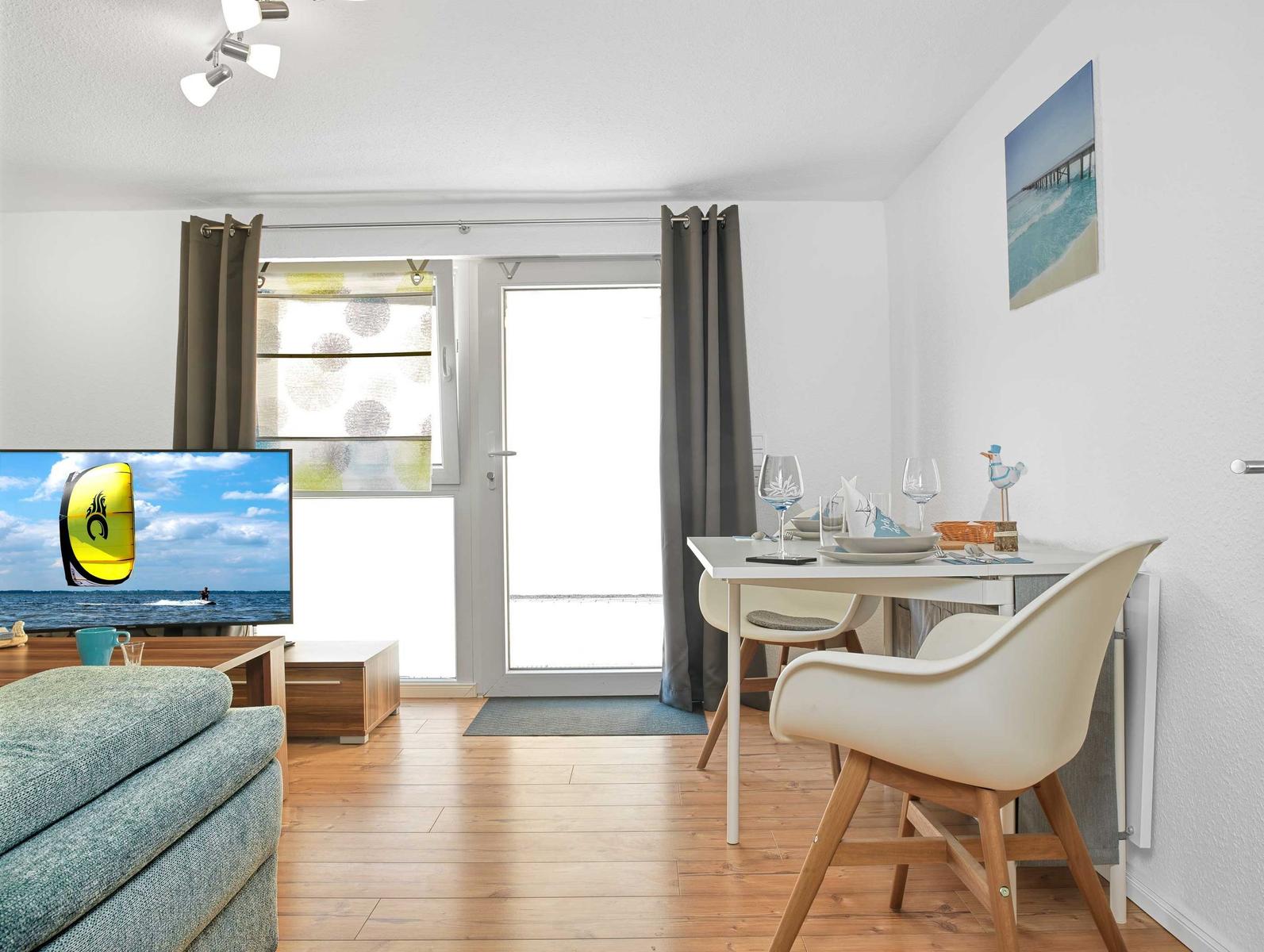 Wohn- und Essbereich mit Fernseher, Tisch, Stühlen und Balkontür.