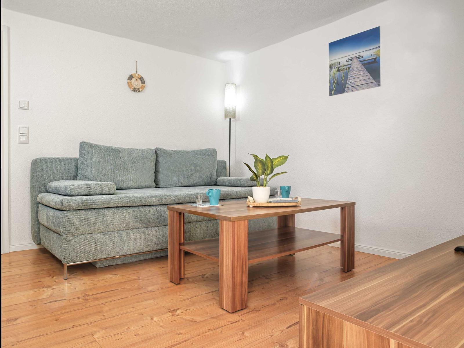 Ein Wohnzimmer mit grauem Sofa, Holztisch und Wandbild.