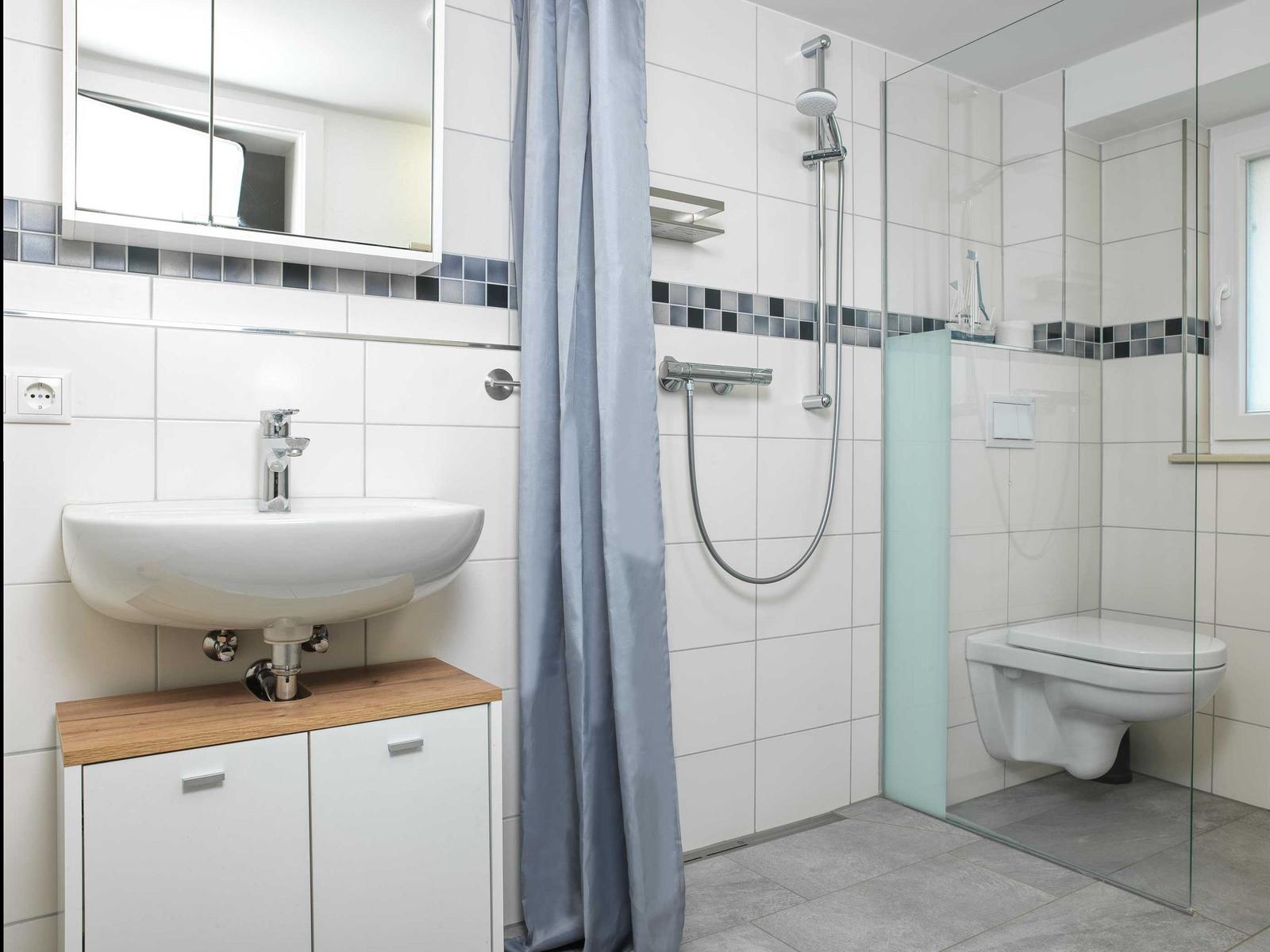 Badezimmer mit Dusche, Toilette und Waschbecken auf Holzunterschrank.