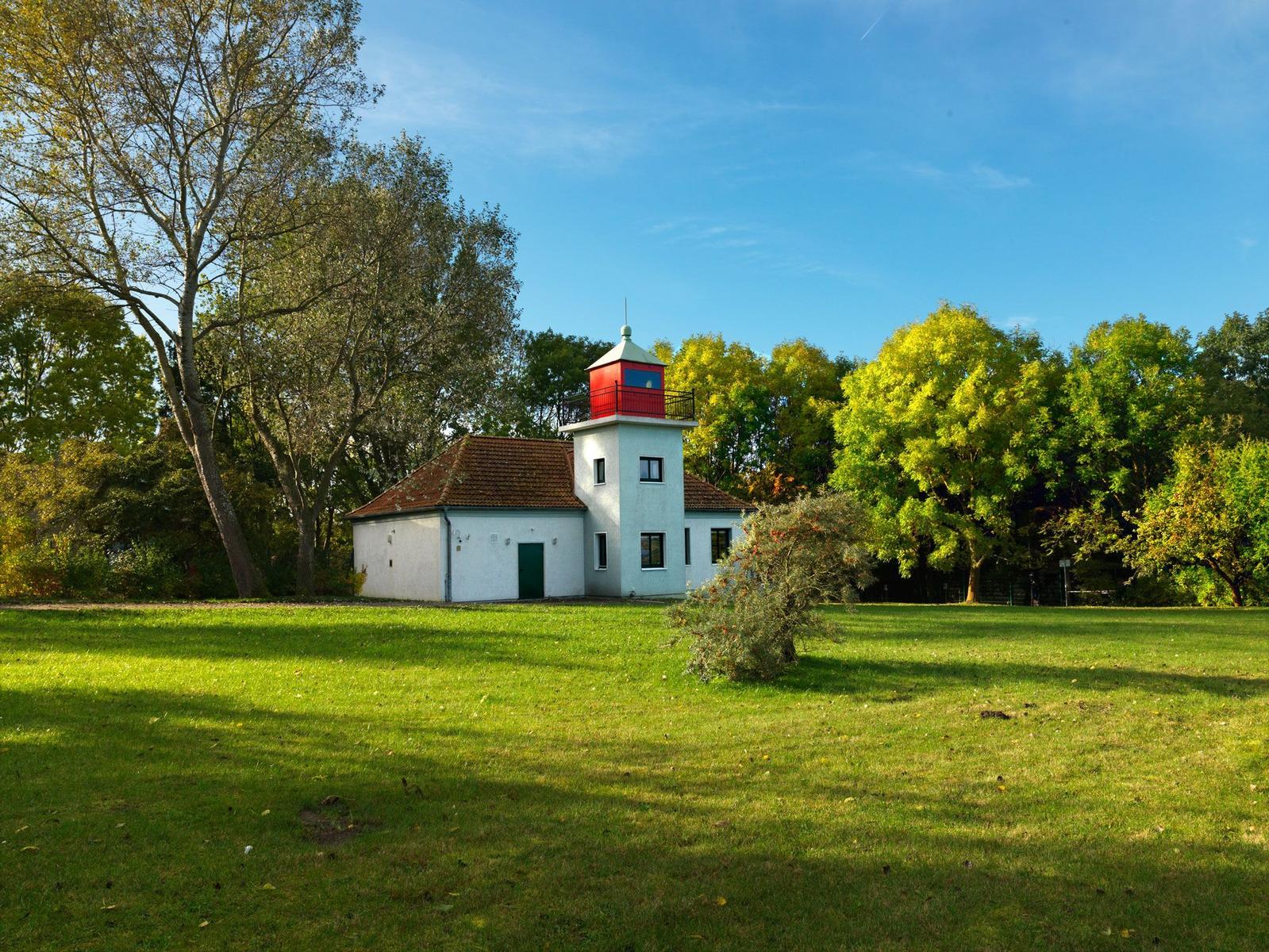 Wohnhaus mit rotem Turm, umgeben von Gras und Bäumen unter blauem Himmel.