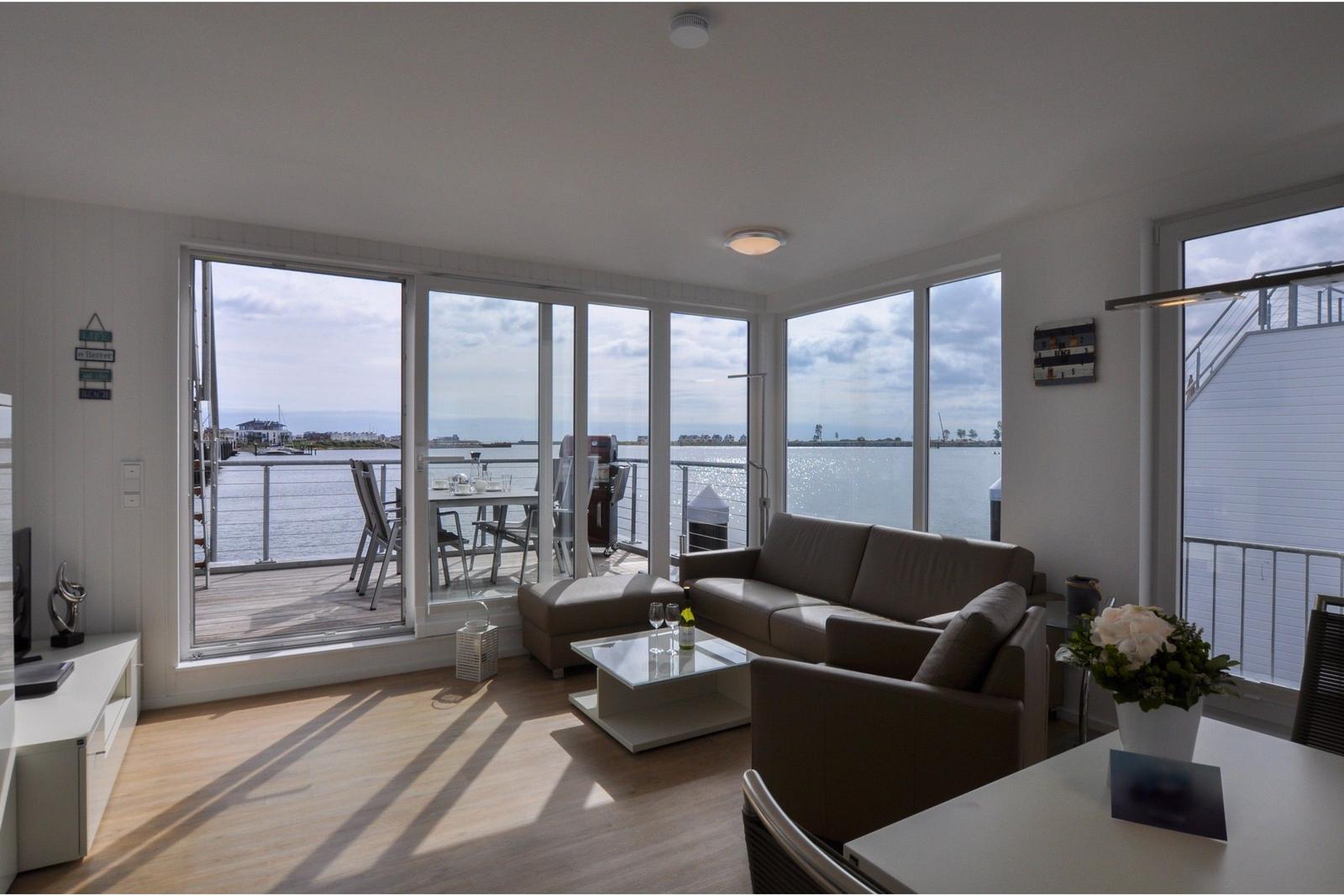 Wohnbereich mit Blick auf Wasser und Terrasse mit Tisch und Stühlen.