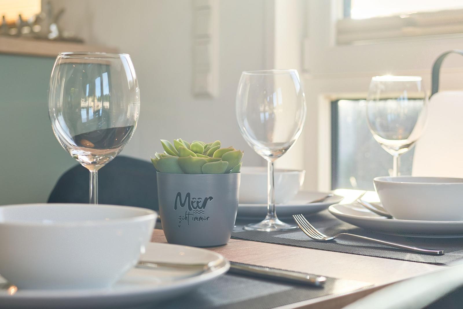 Tisch gedeckt mit Gläsern, Tellern und einer Pflanze.
