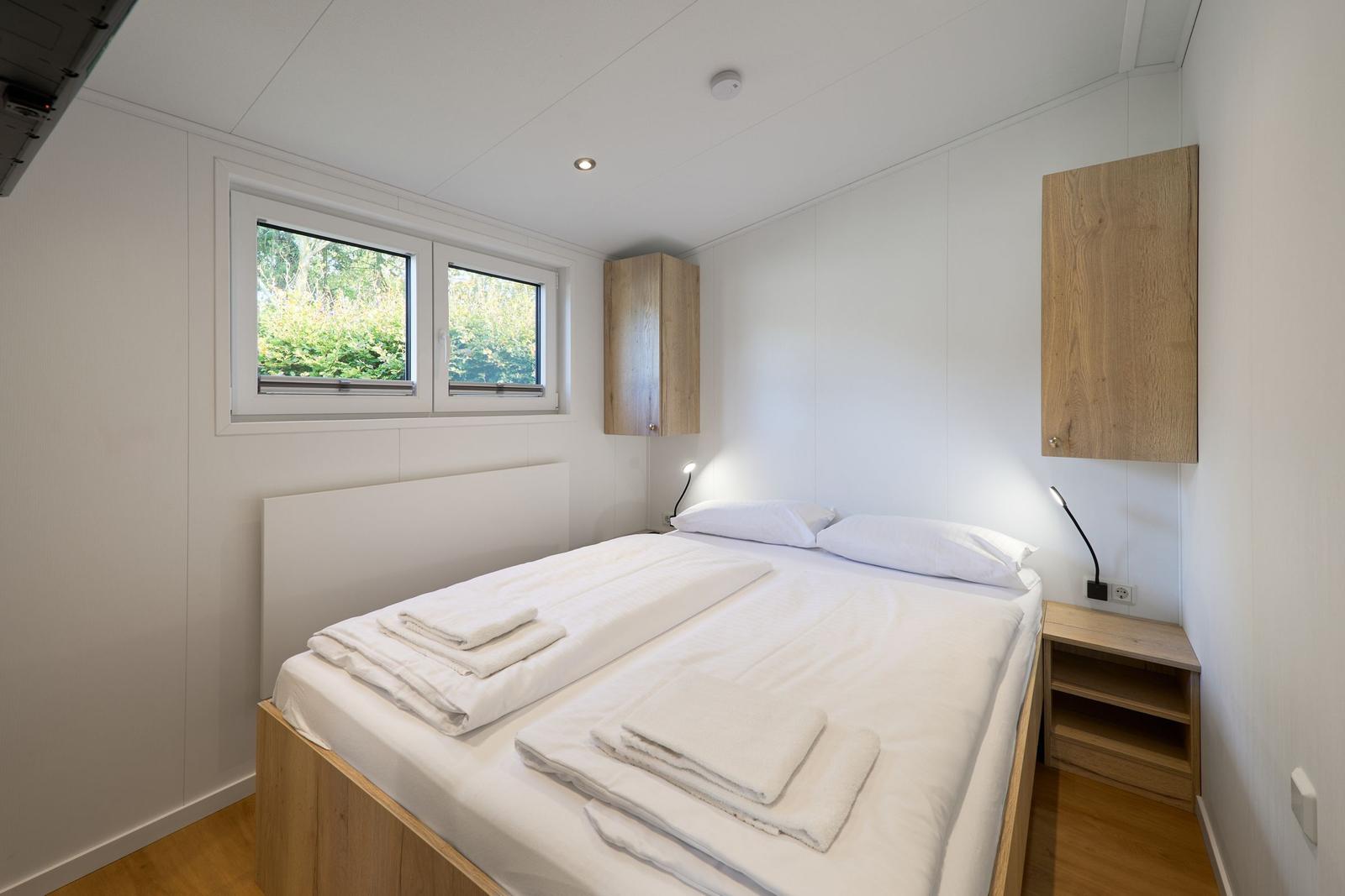 Schlafzimmer mit Doppelbett, Holzmöbeln und Fenster mit Blick auf Grün.