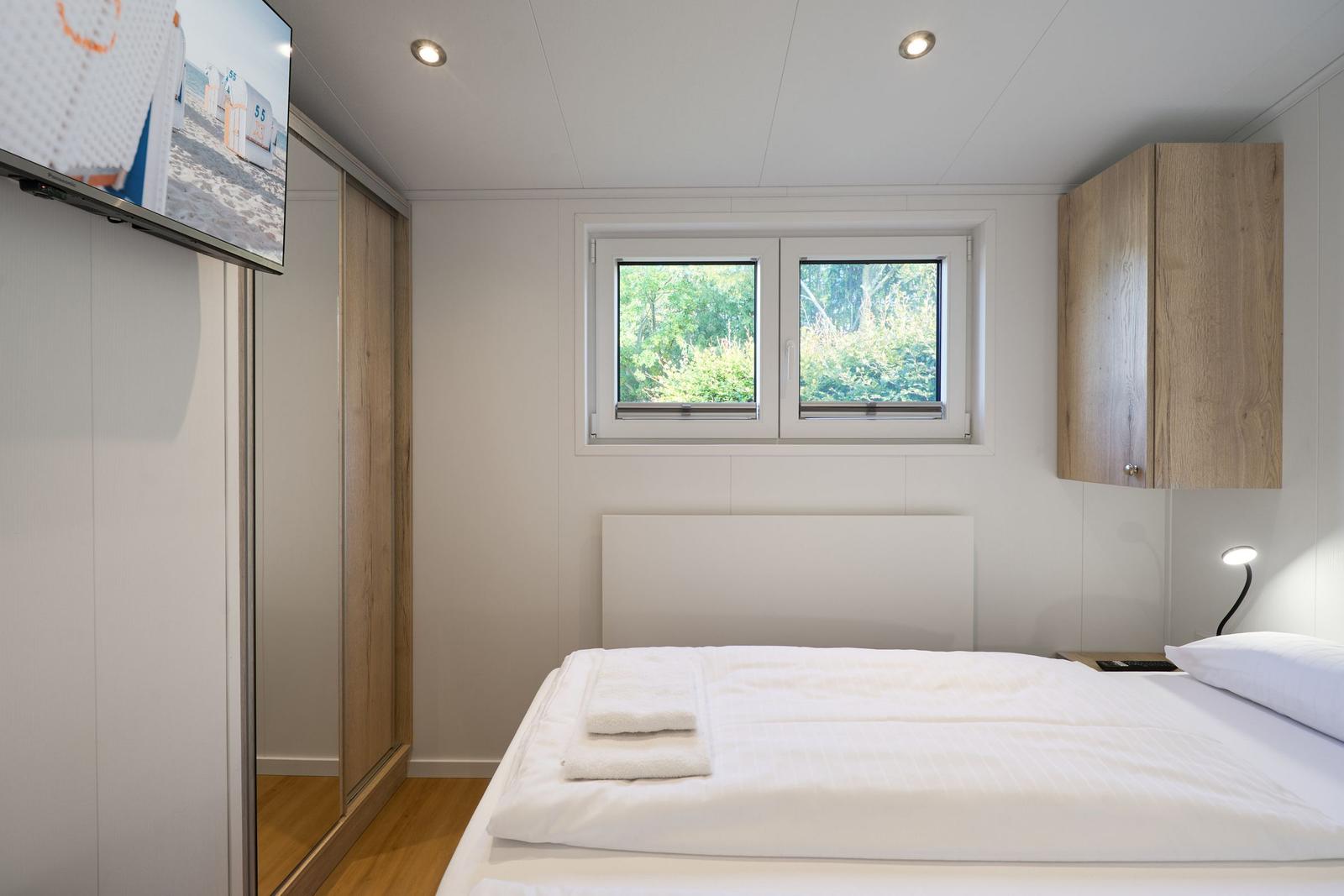 Schlafzimmer mit Bett, Fenster, Schrank und TV.