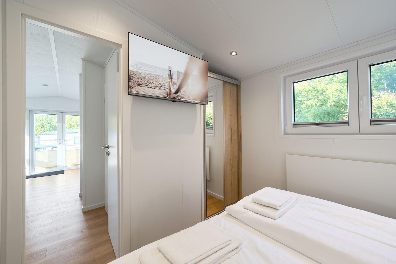 Schlafzimmer mit Bett, TV und Fenster. Durchgang zur Wohnfläche.