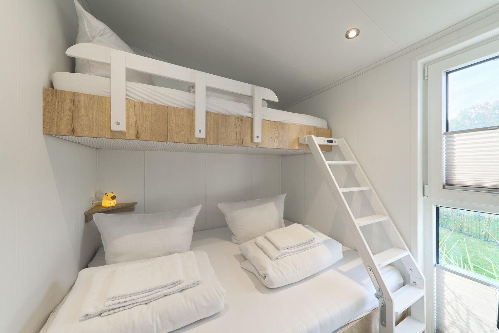 Zimmer mit Doppelbett und Hochbett mit Leiter und Fenster.