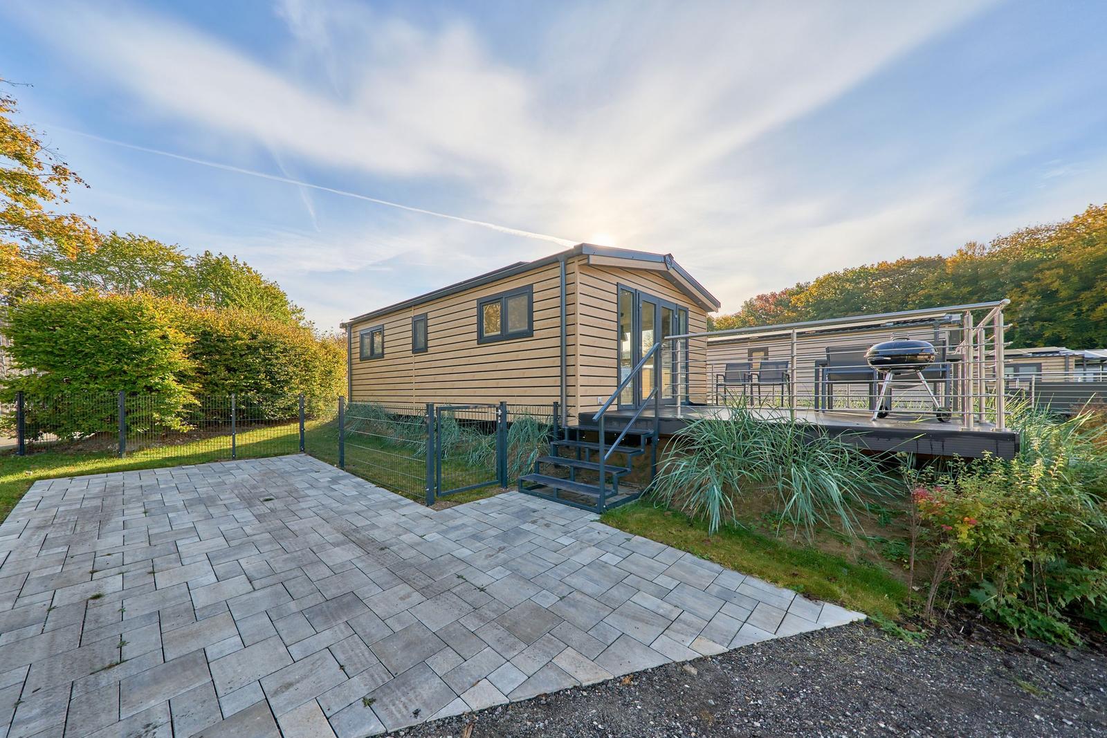 Holzhaus mit Terrasse, Grill und gepflastertem Hof im Wald.