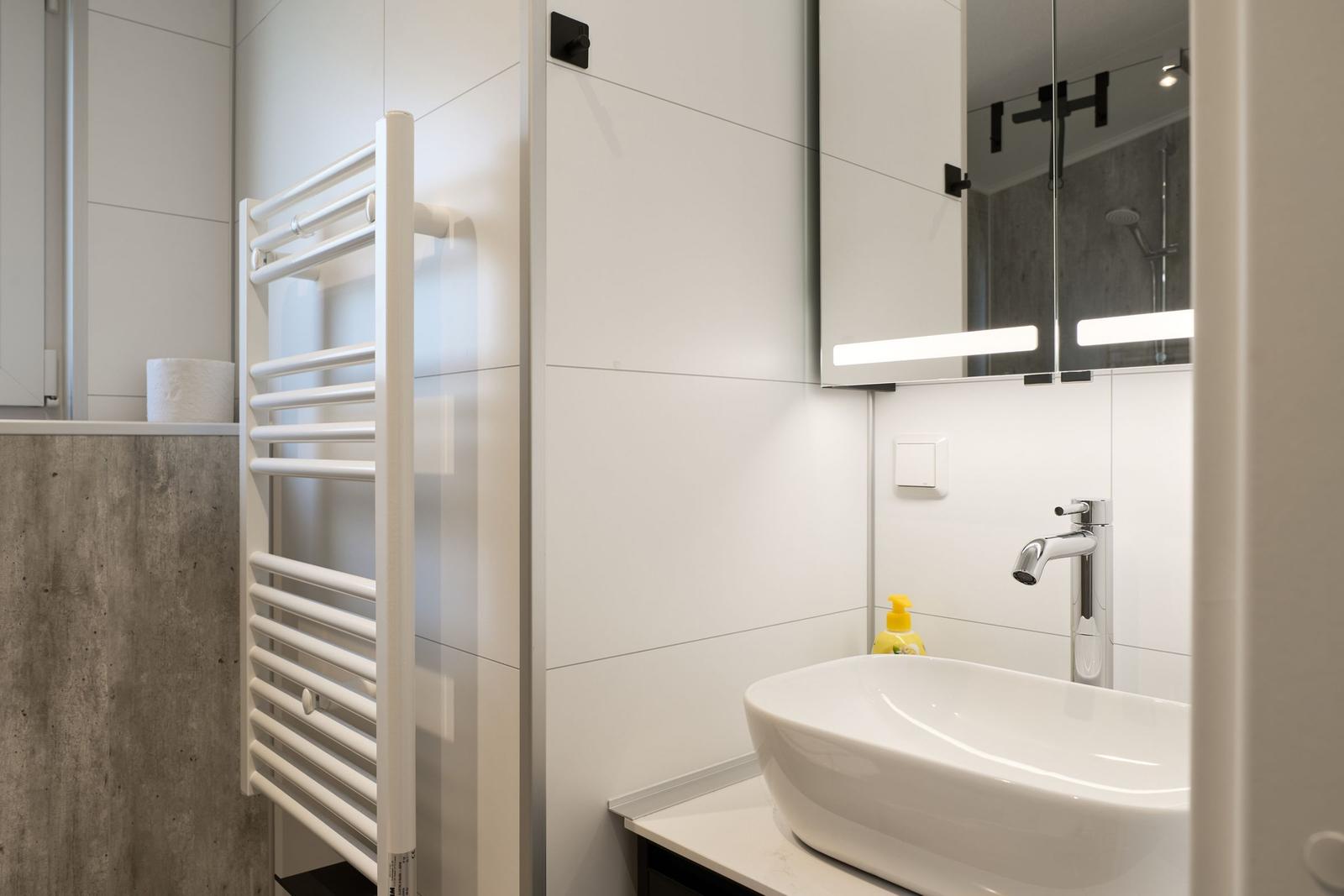 Badezimmer mit Waschbecken, Spiegel und Heizkörper.