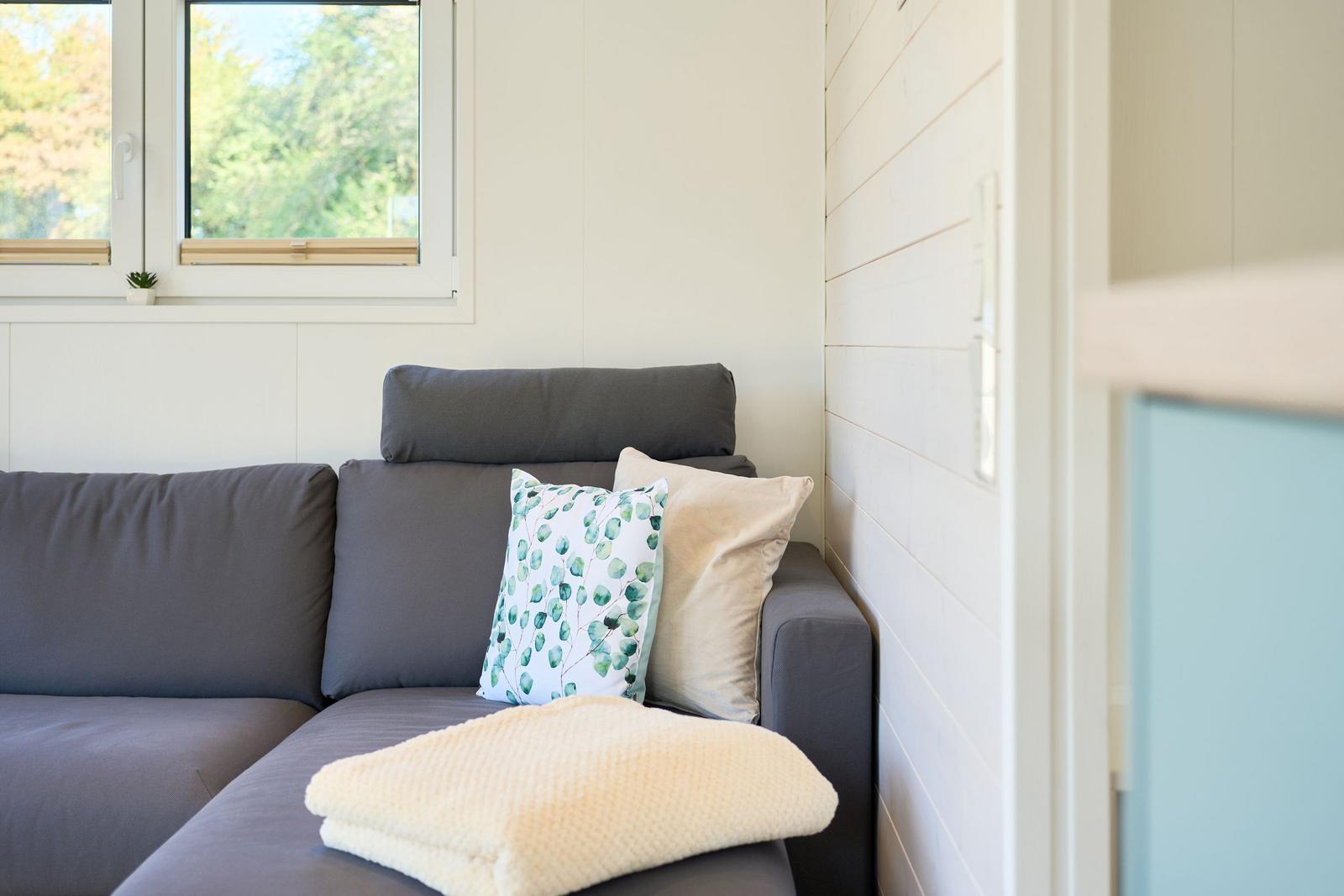 Graße Couch mit Kissen und Decke vor Fenster mit Blick auf Bäume