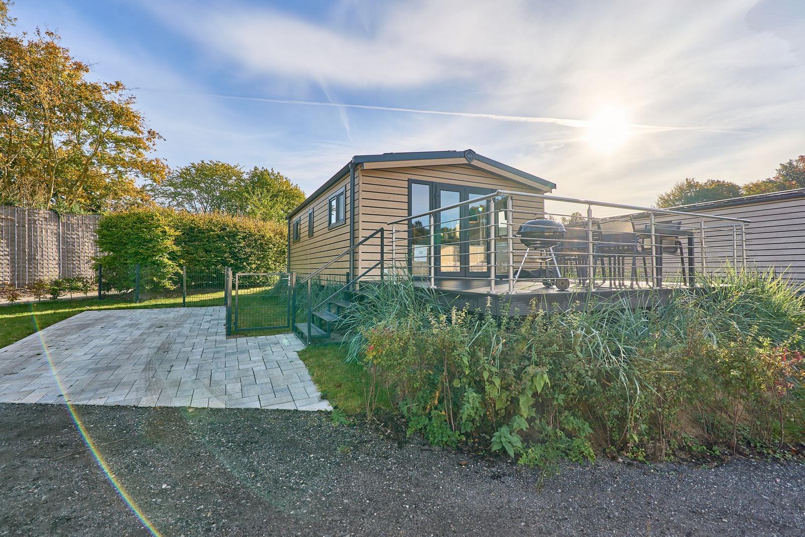 Holzhaus mit Terrasse, Grill und Garten. Zugang über gepflasterten Weg.