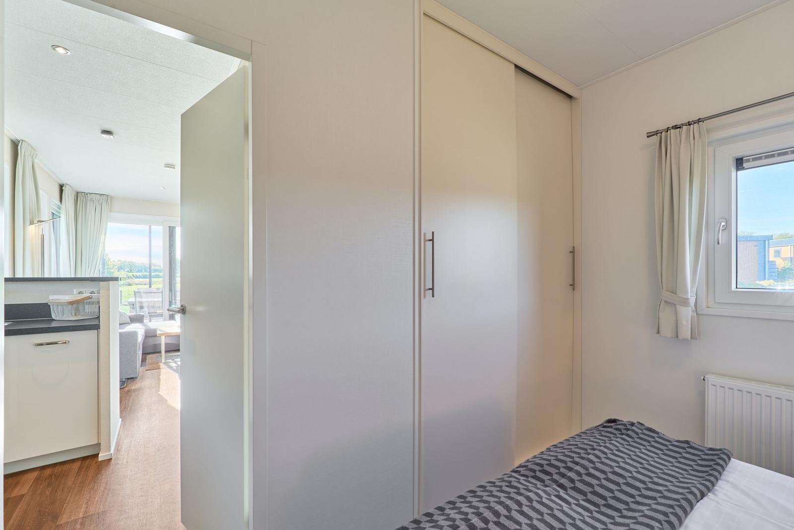 Schlafzimmer mit Bett, Kleiderschrank und Fenster. Durchgang zur Küche und Wohnfläche.