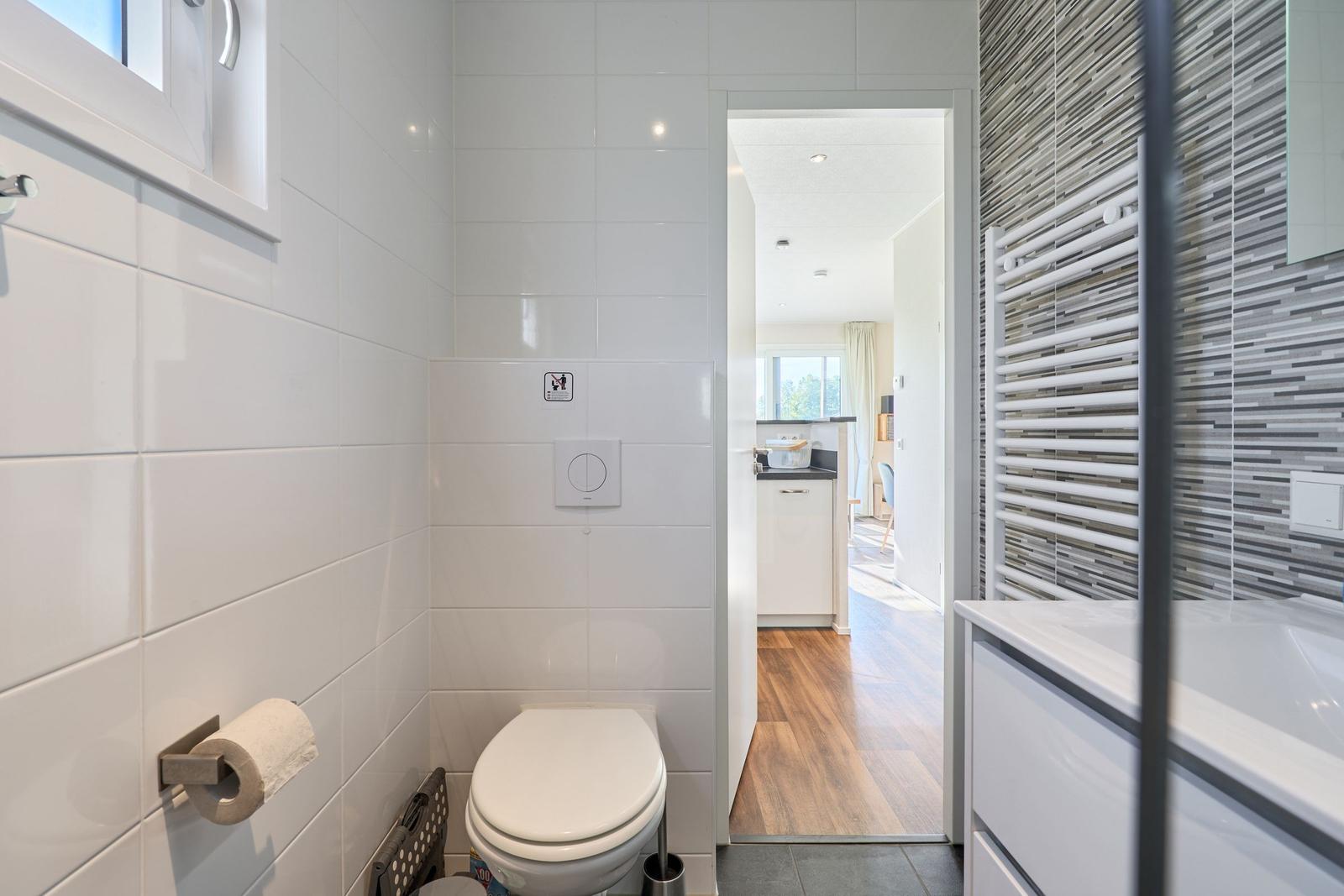 Badezimmer mit Toilette, Waschtisch und Heizung. Blick in die Küche.