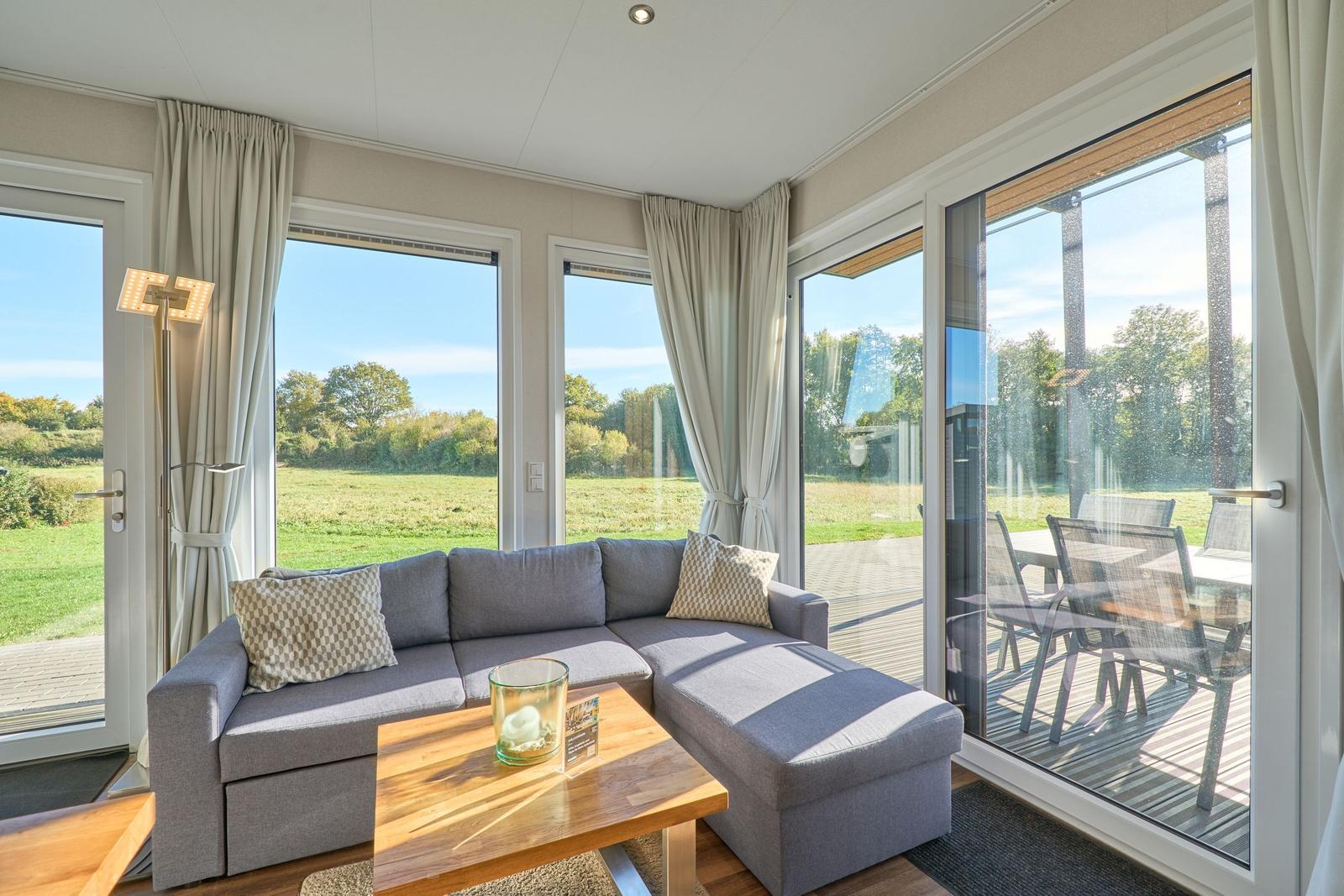 Wohnzimmer mit Sofa, Tisch und großen Fenstern zur Terrasse.