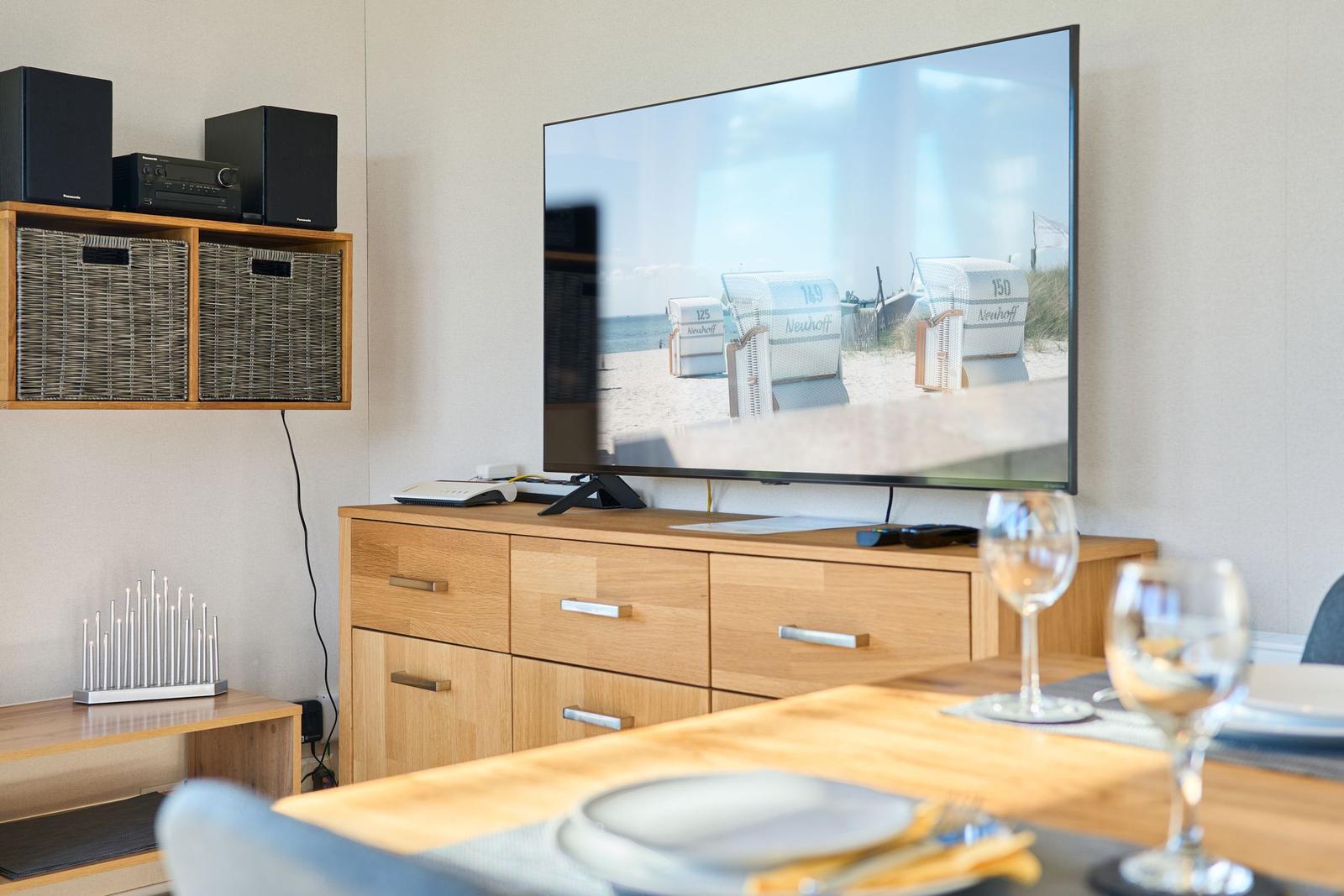 TV zeigt Strand, Esstisch mit Gläsern und Holzmöbeln