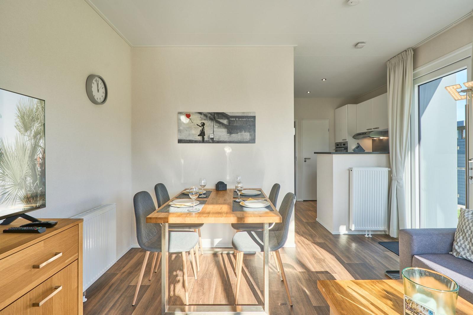 Essbereich mit Tisch, Stühlen und Wandbild. Küche und Wohnbereich im Hintergrund.