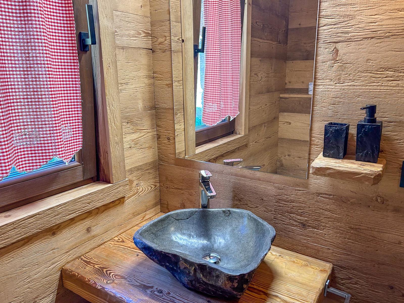 Bad mit Steinwaschbecken, Holzwand und Spiegel mit rotem Gittervorhang.