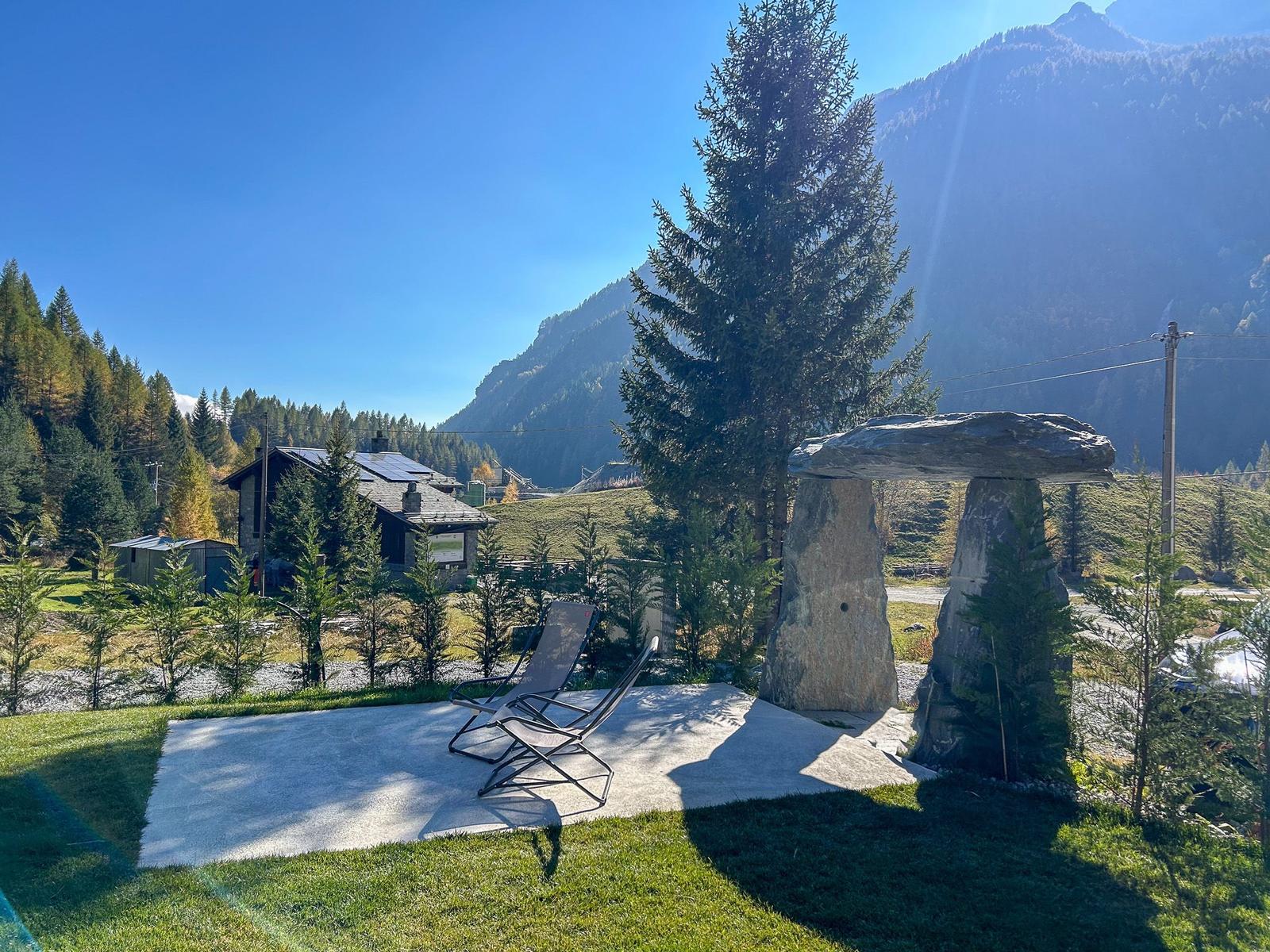 Terrasse mit Liegestuhl und Steinmonolithen. Blick auf Berg und Wald.