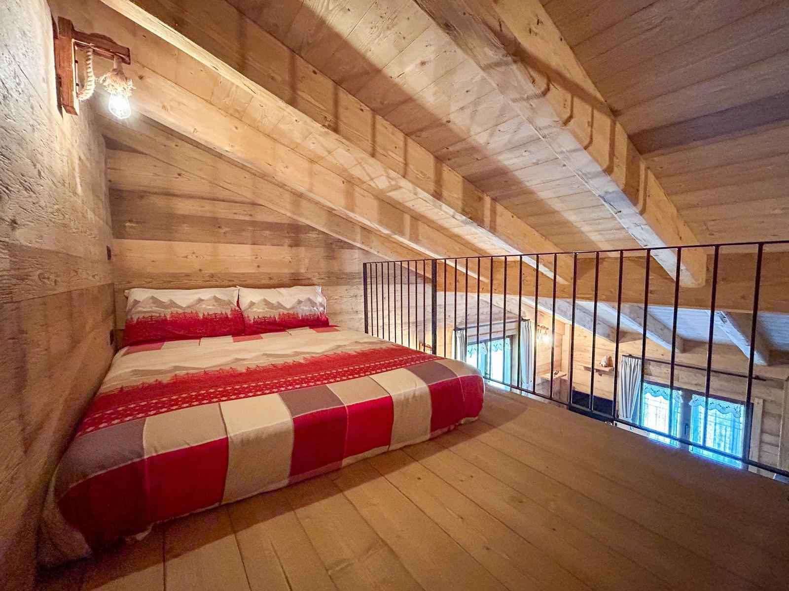 Schlafzimmer mit Holzdecke und -boden, Bett mit Muster, Geländer und Wandlampe.