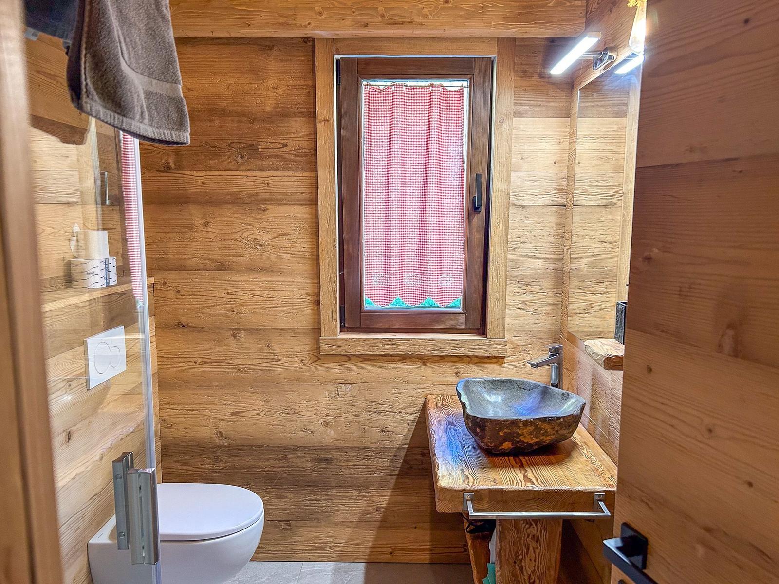 Holzbadezimmer mit Waschbecken, Toilette und Fenster mit rotem Vorhang.