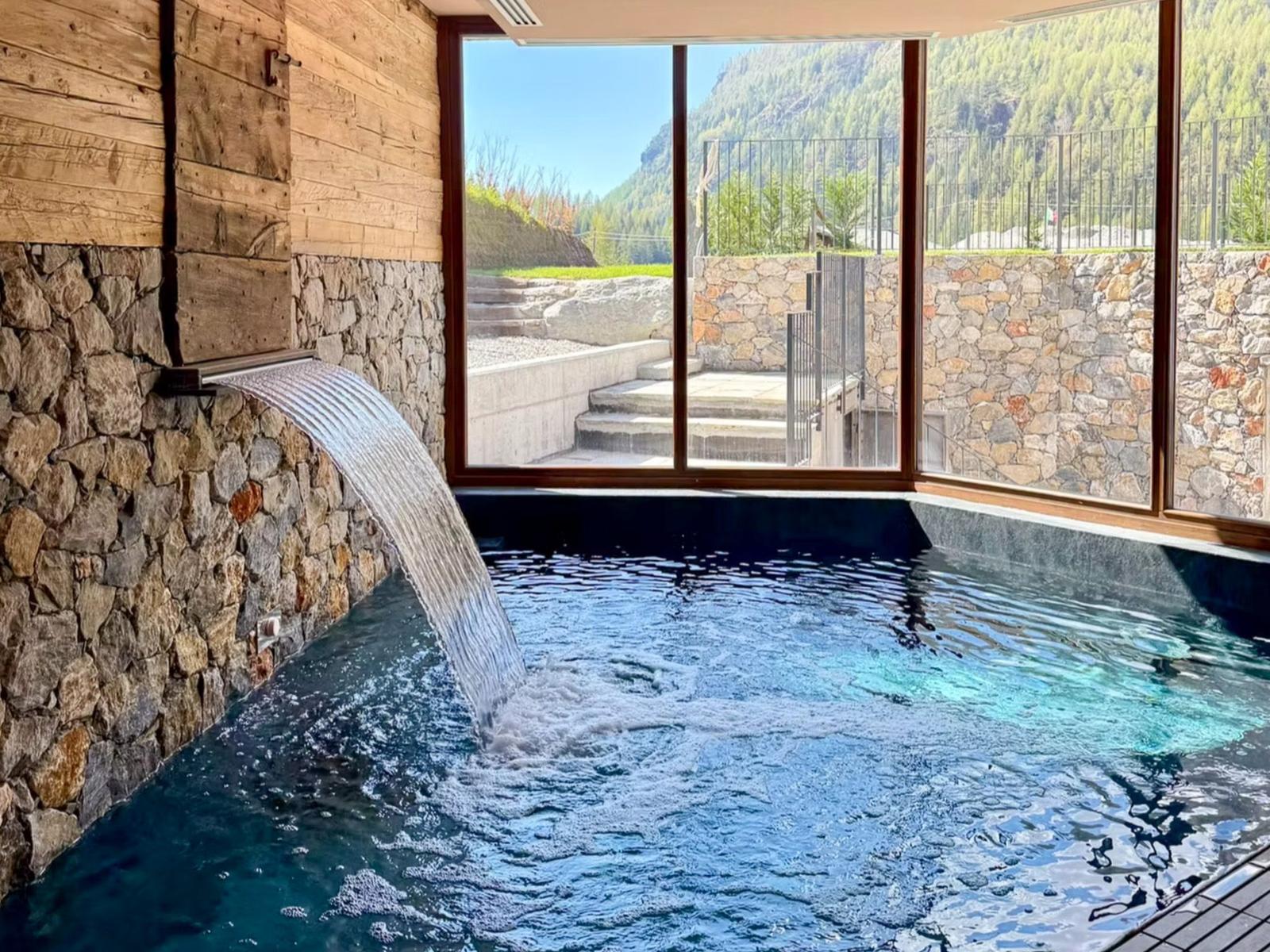 Indoor-Pool mit Wasserfall und Bergblick durch große Fenster.