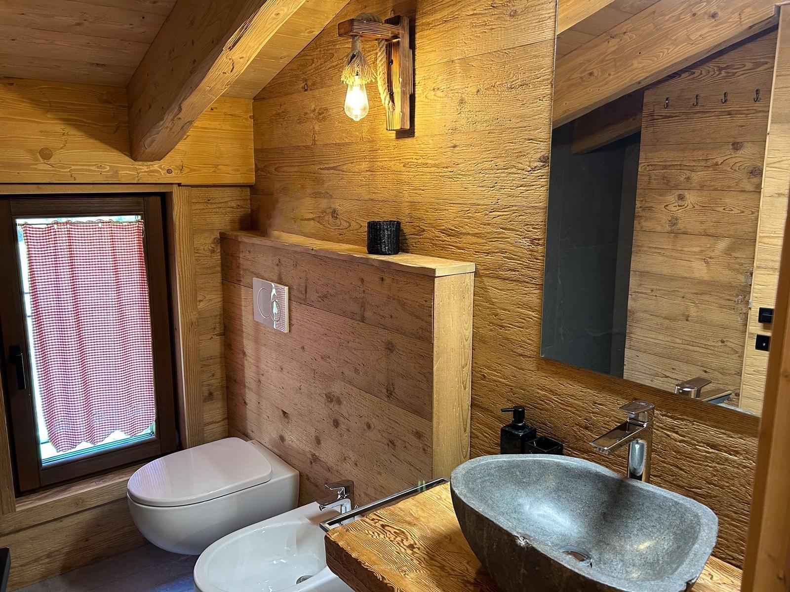 Holzbadezimmer mit Waschbecken, Toilette und Fenster mit kariertem Vorhang.