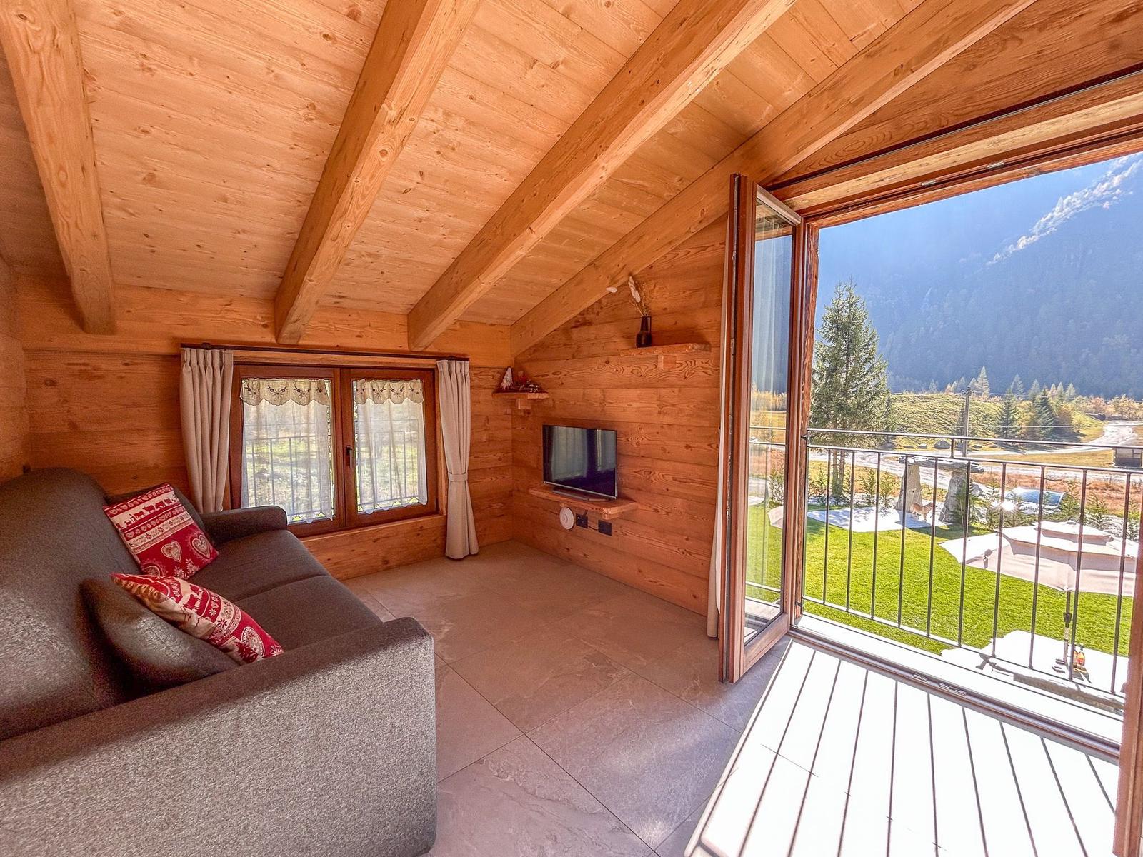 Wohnzimmer mit Sofa, Fernseher und Balkon mit Bergblick.