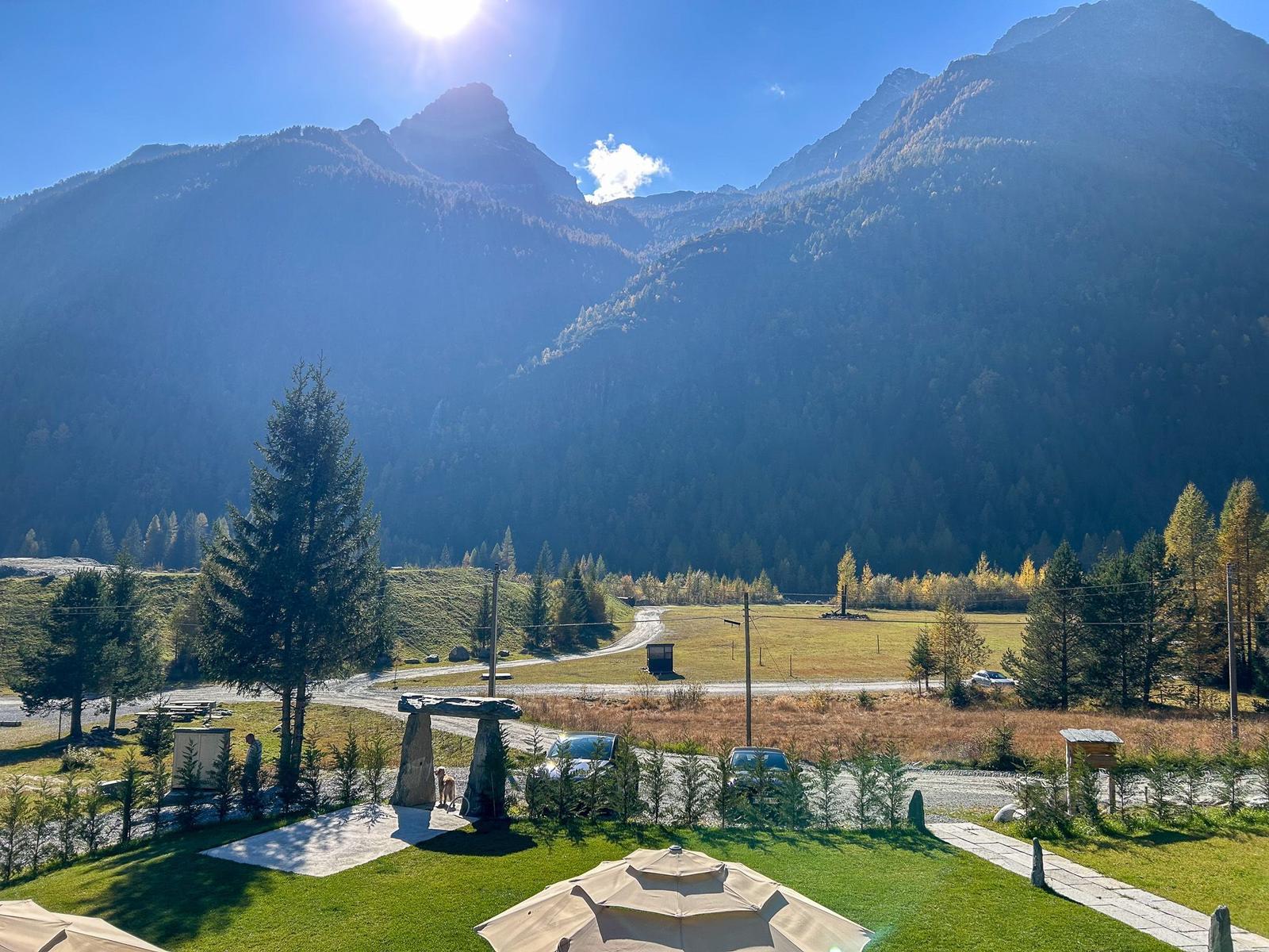 Grünes Gelände mit Steinmonument, Wegen und Bergen im Hintergrund.