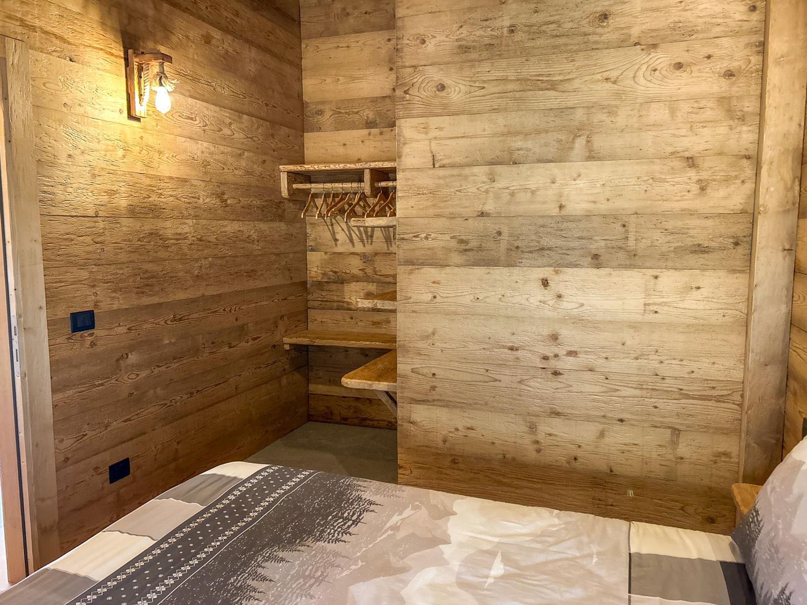 Schlafzimmer mit Holzwand, Kleiderschrank und Bett mit Musterdecke.