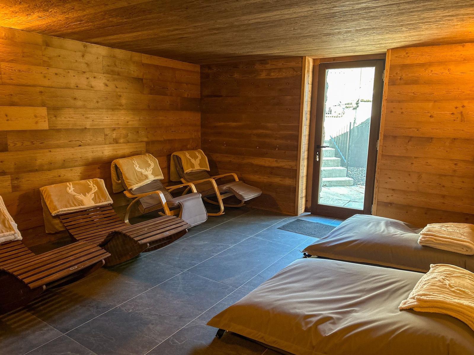 Raum mit Holzwand, Liegen und Bett. Tür führt nach draußen.