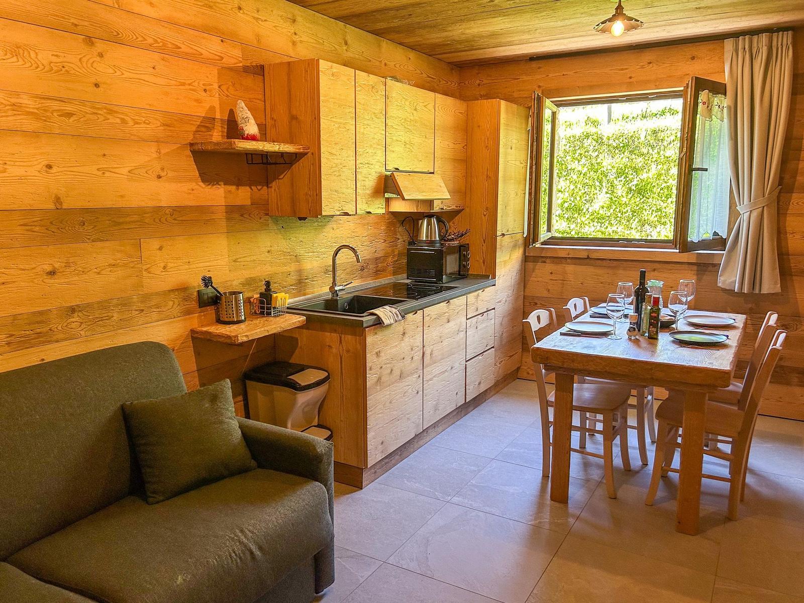 Küche mit Essbereich und Sofa. Holzwände und -möbel. Fenster mit Blick auf Grün.