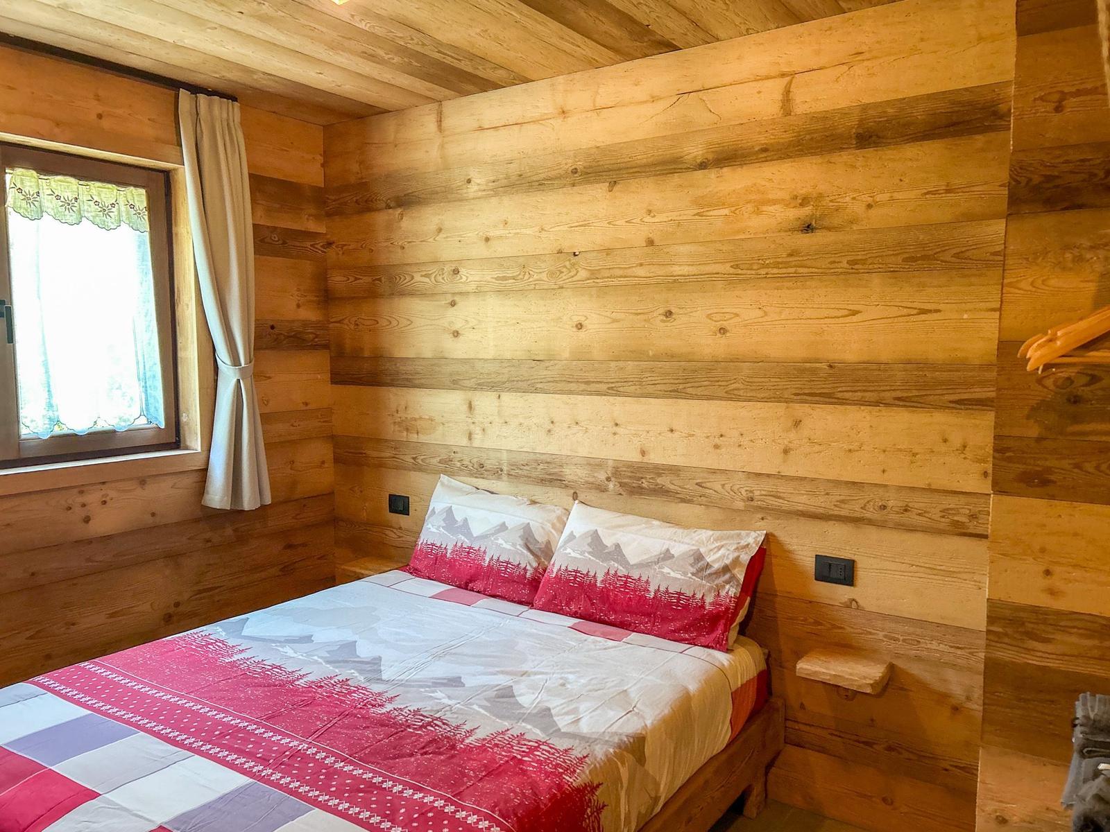 Schlafzimmer mit Holzwand und Bett mit Bergmotiv-Bettwäsche.