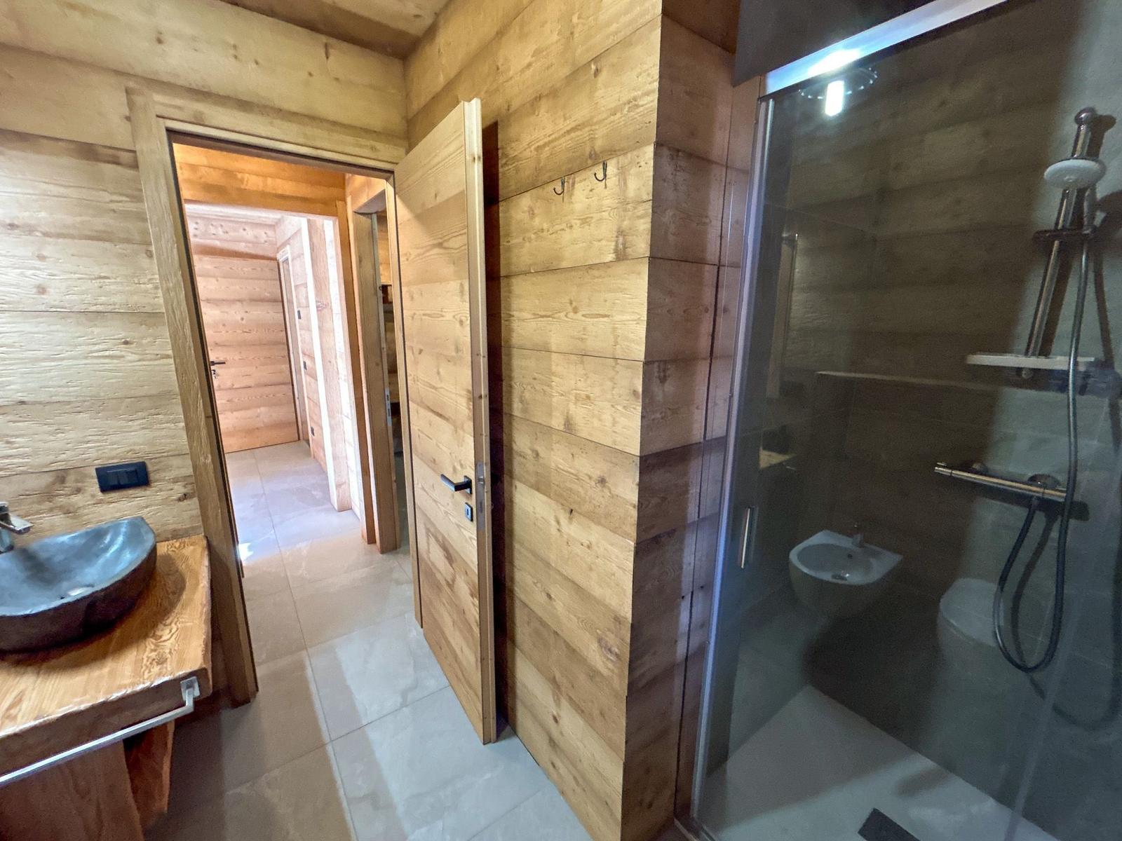 Badezimmer mit Holzwand, Dusche, Waschbecken und Toilette.