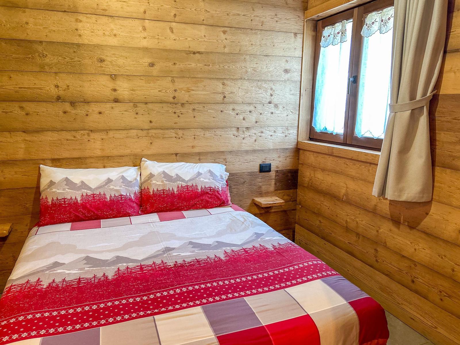 Schlafzimmer mit Holzwand und Fenster mit Vorhängen.