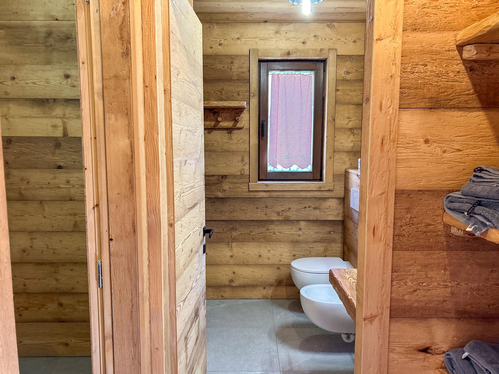 Holzbadezimmer mit Toilette, Waschbecken und Fenster mit rotem Gitter.
