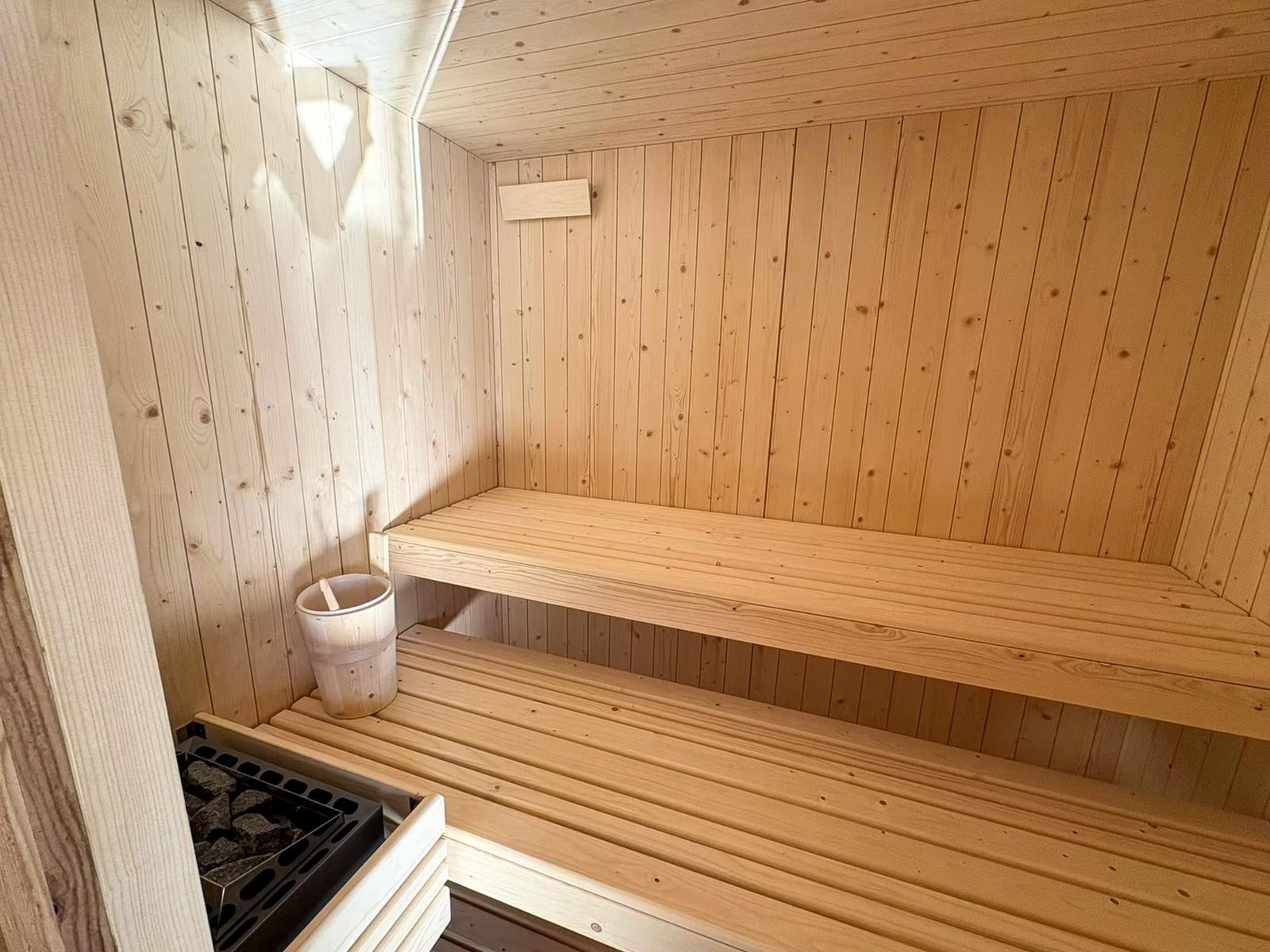 Sauna mit Holzbank und Holzwanne. Holzwände und Holzdecke. Steinmulde mit Steinen.