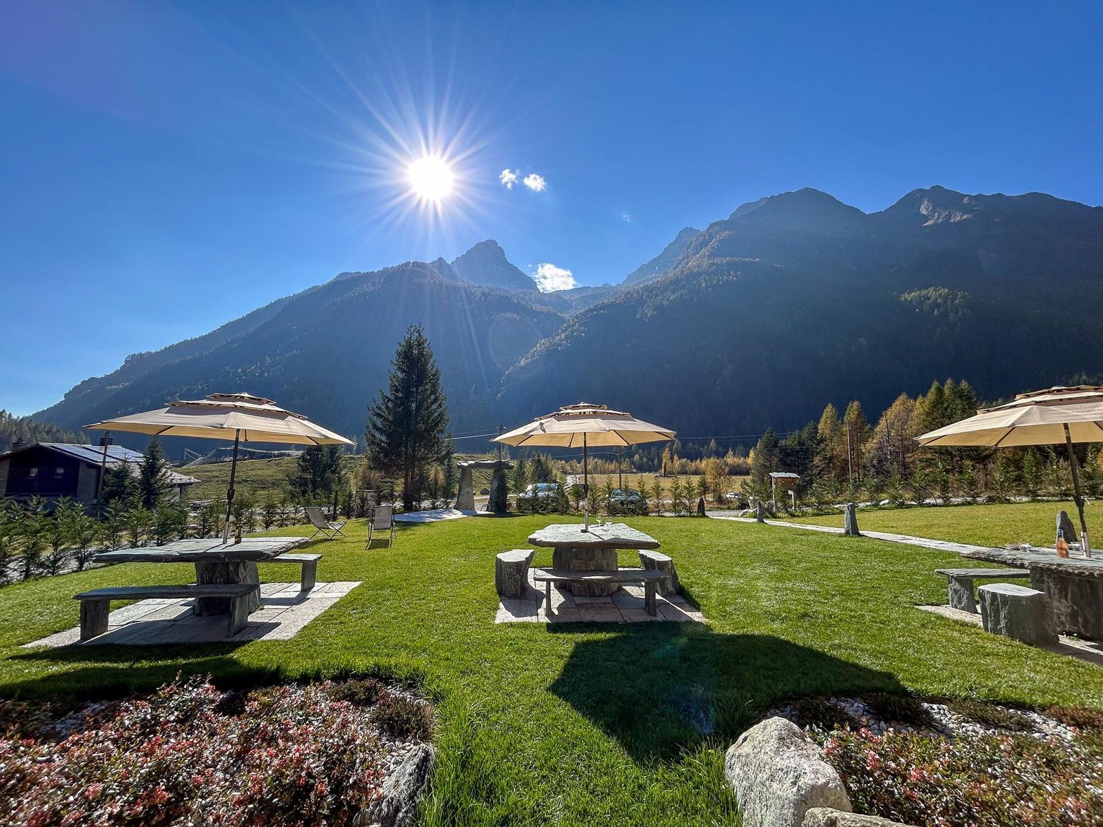 Großer Garten mit Steinbänken, Sonnenschirmen und Bergblick.