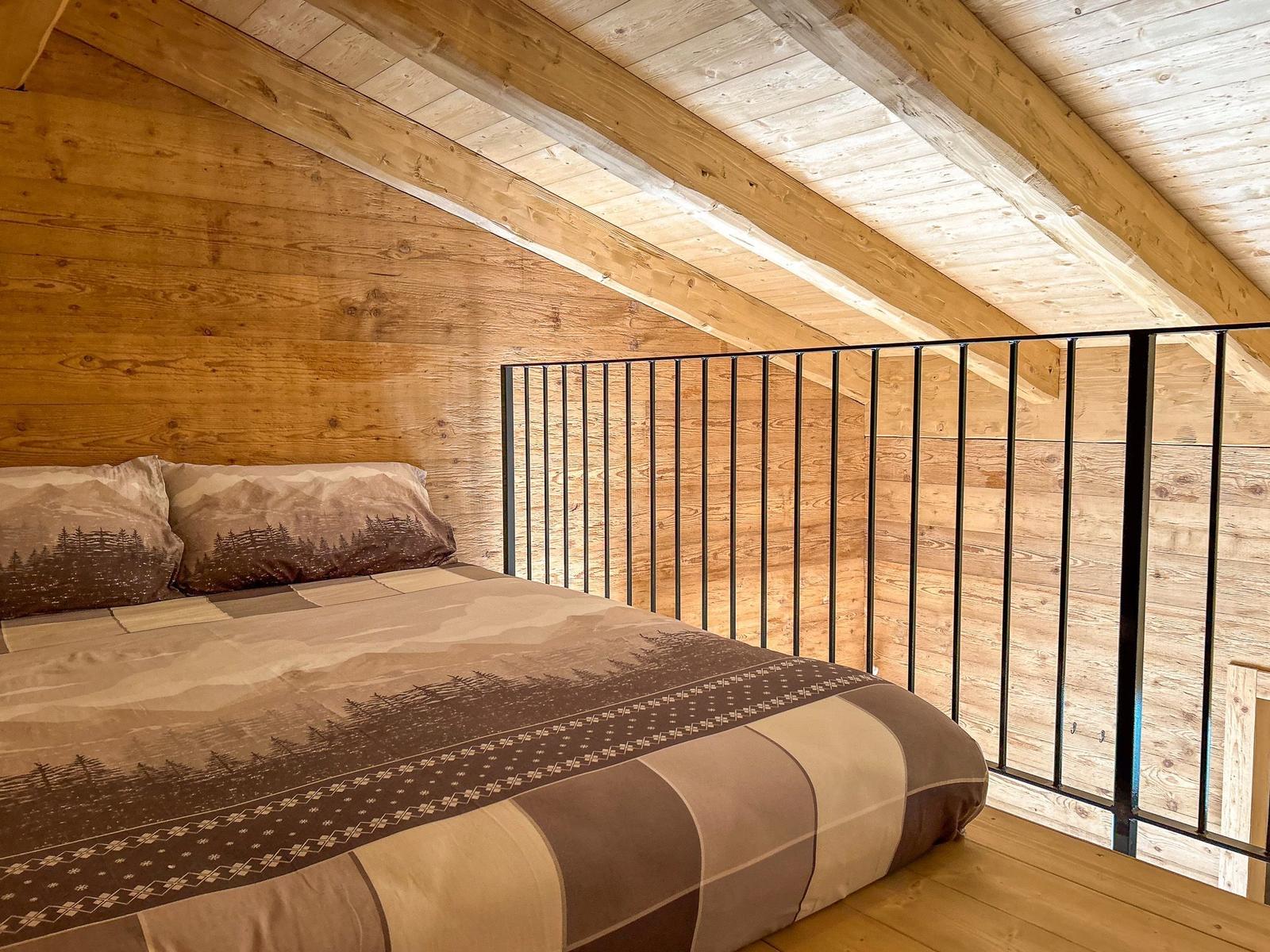 Schlafzimmer mit Holzwand und Dachschrägen, Bett mit Bergmotiv.