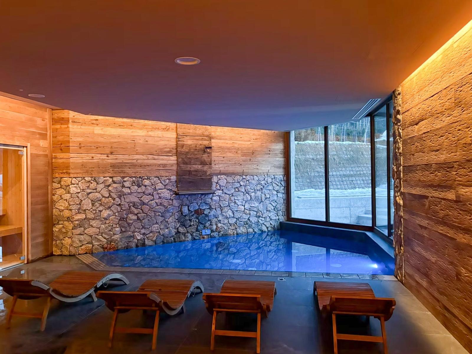 Innenpool mit Holzwand und Steinmauer, Liegestühle und großes Fenster