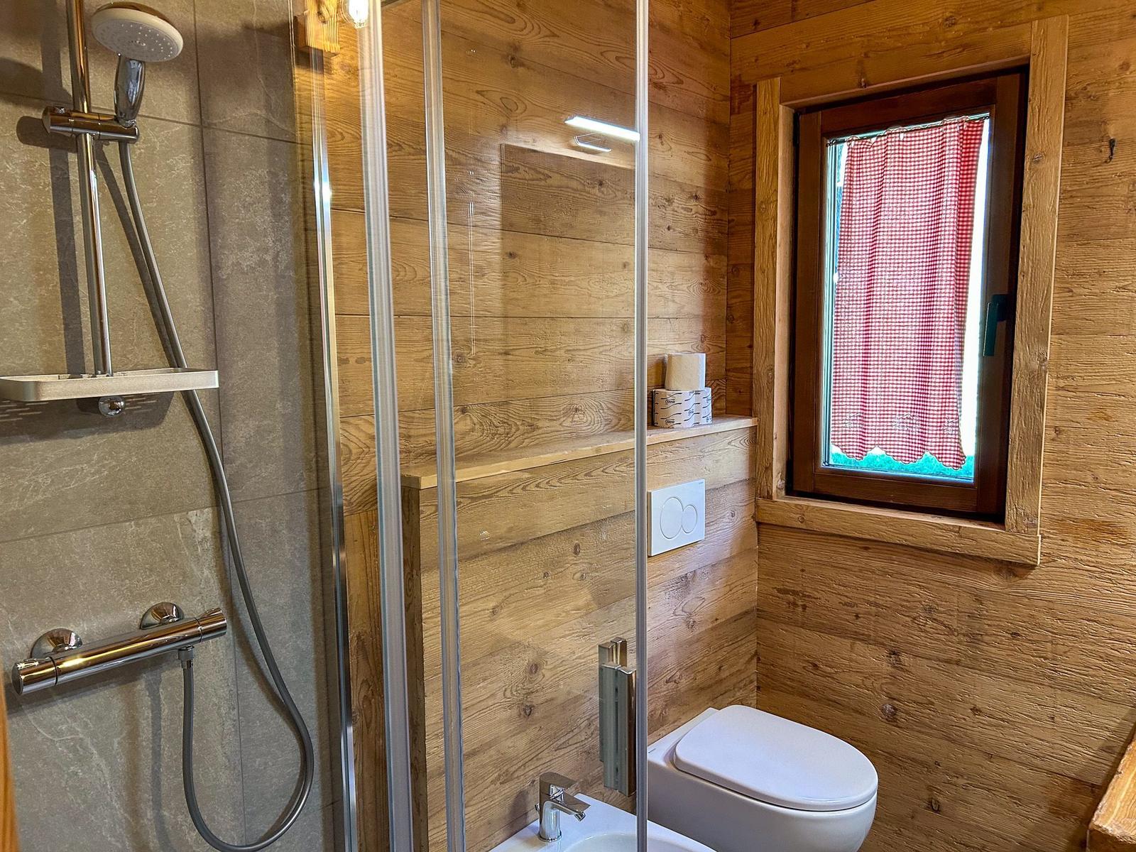 Bad mit Dusche, Toilette und Fenster mit rotem Gitterstoff.