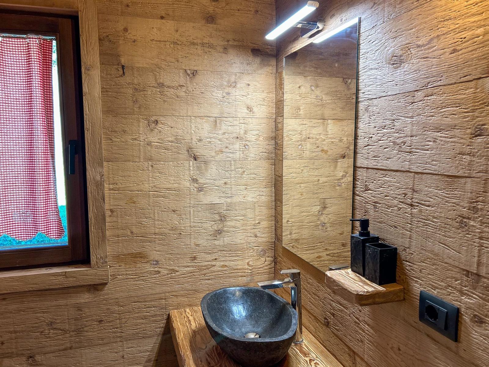 Bad mit Steinwaschbecken, Holzwand und Spiegel mit Licht