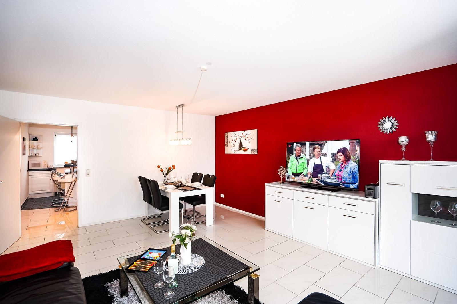 Wohn- und Essbereich mit roter Wand, TV und Esstisch.